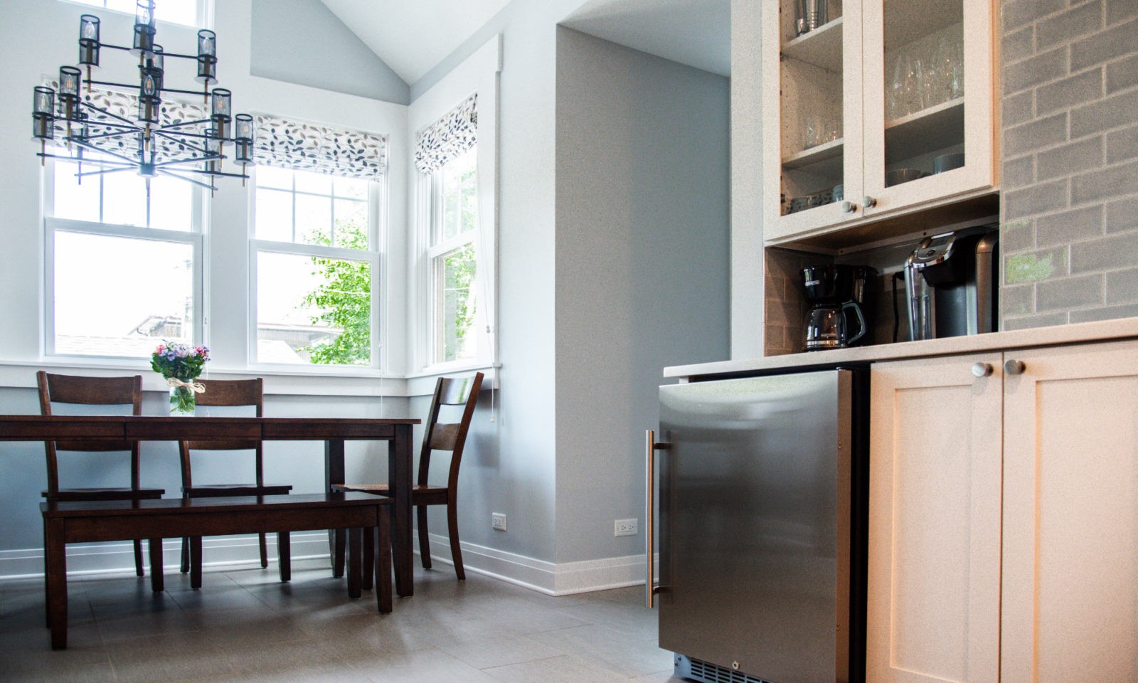 Newly renovated kitchen with glass cabinet doors, stainless steel appliances, gray tile backsplash, chandelier, and a dark wooden table