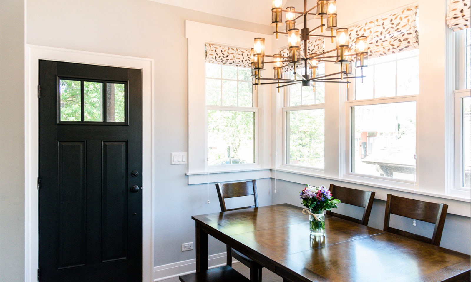 Newly renovated kitchen with bright windows, wooden kitchen table, dark statement door, and wooden chandelier