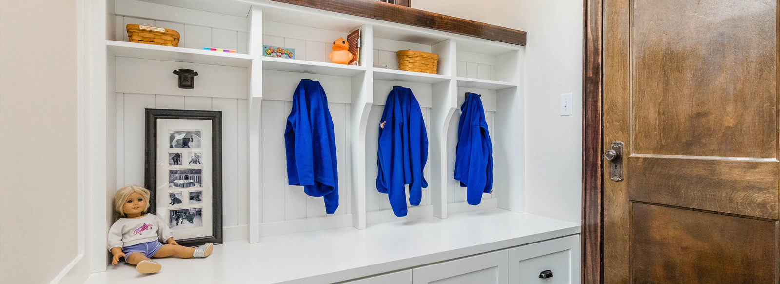 WHITE MUDROOM BUILTINS WITH BLUE JACKETS ON COAT HOOKS