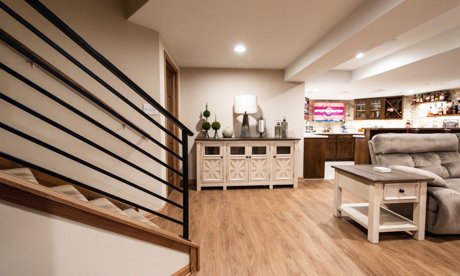 view of basement remodel at bottom of stairs with metal rail