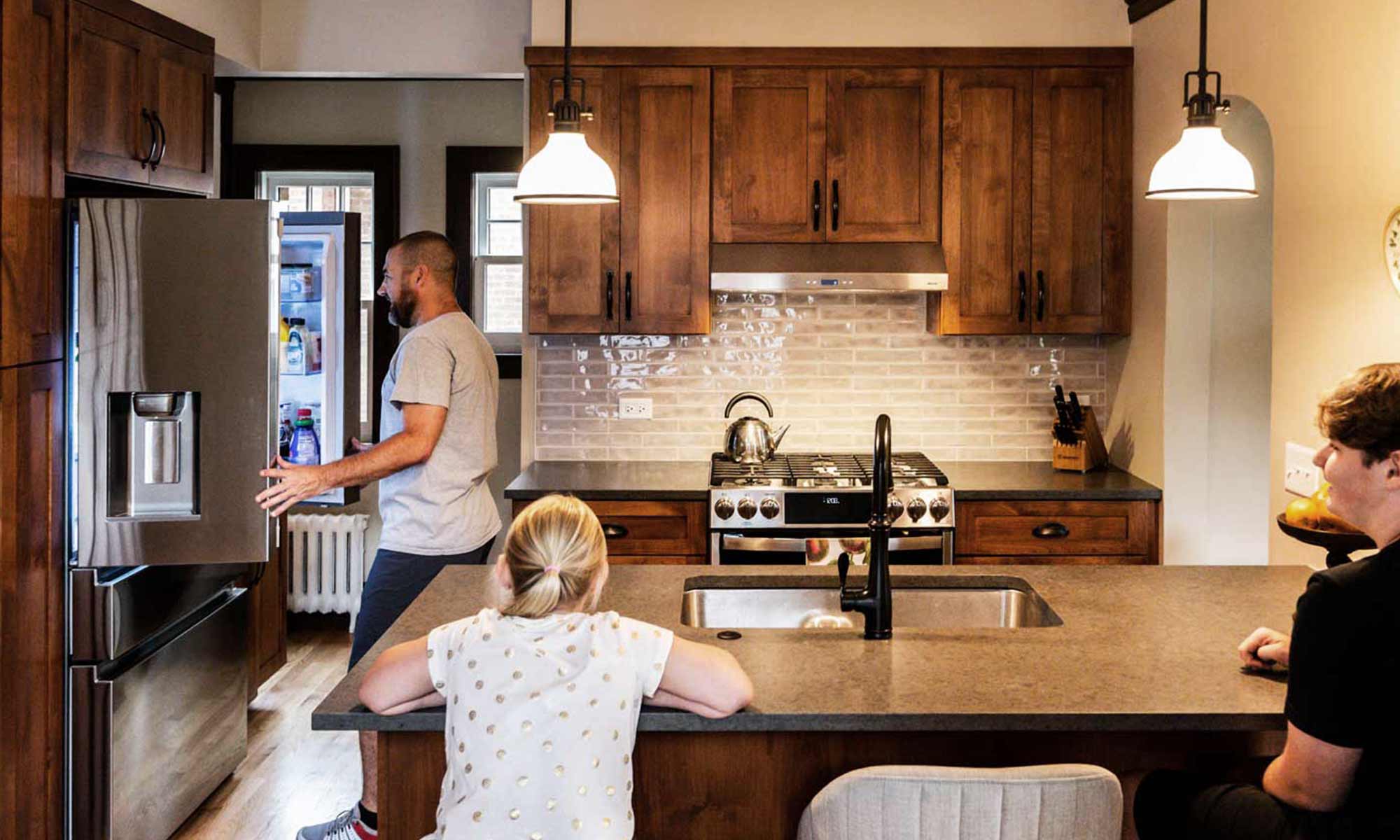 father and daughter gathered in newly remodeled kitchen with dark wood cabinets with dad opening fridge