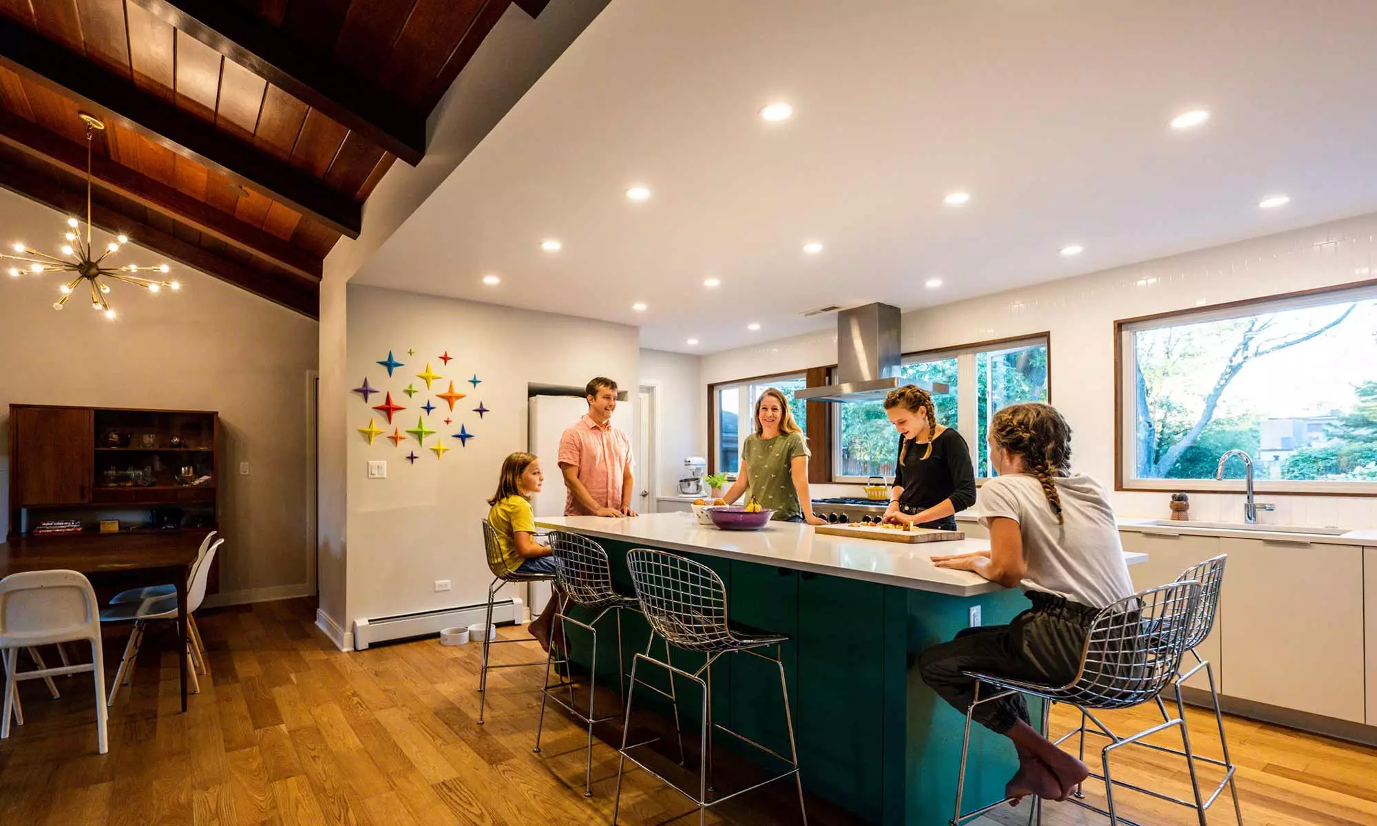 family standing around a green kitchen island in a mid century modern luxury addition wiuth sun coming through windows