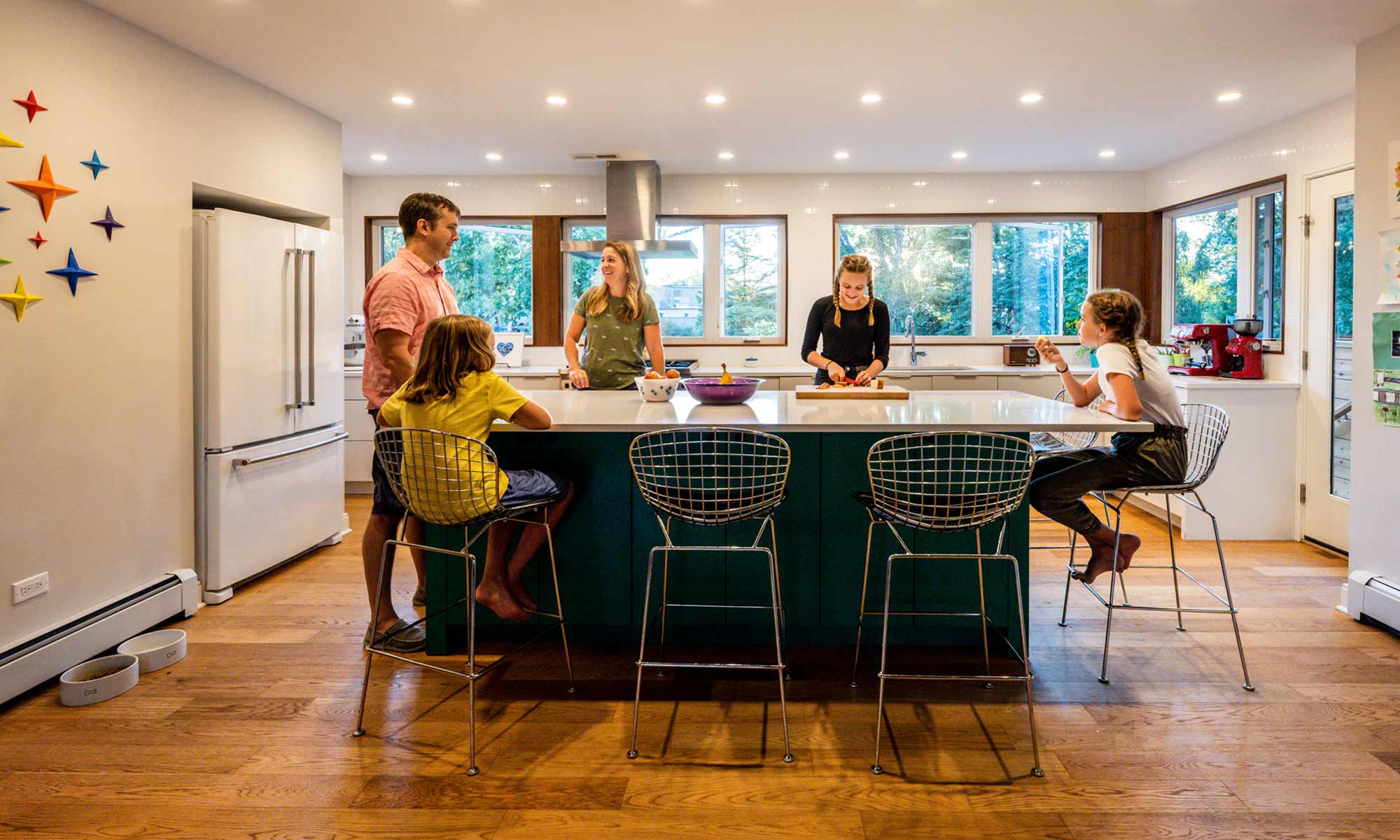 family standing around a green kitchen island in a mid century modern luxury addition wiuth sun coming through windows