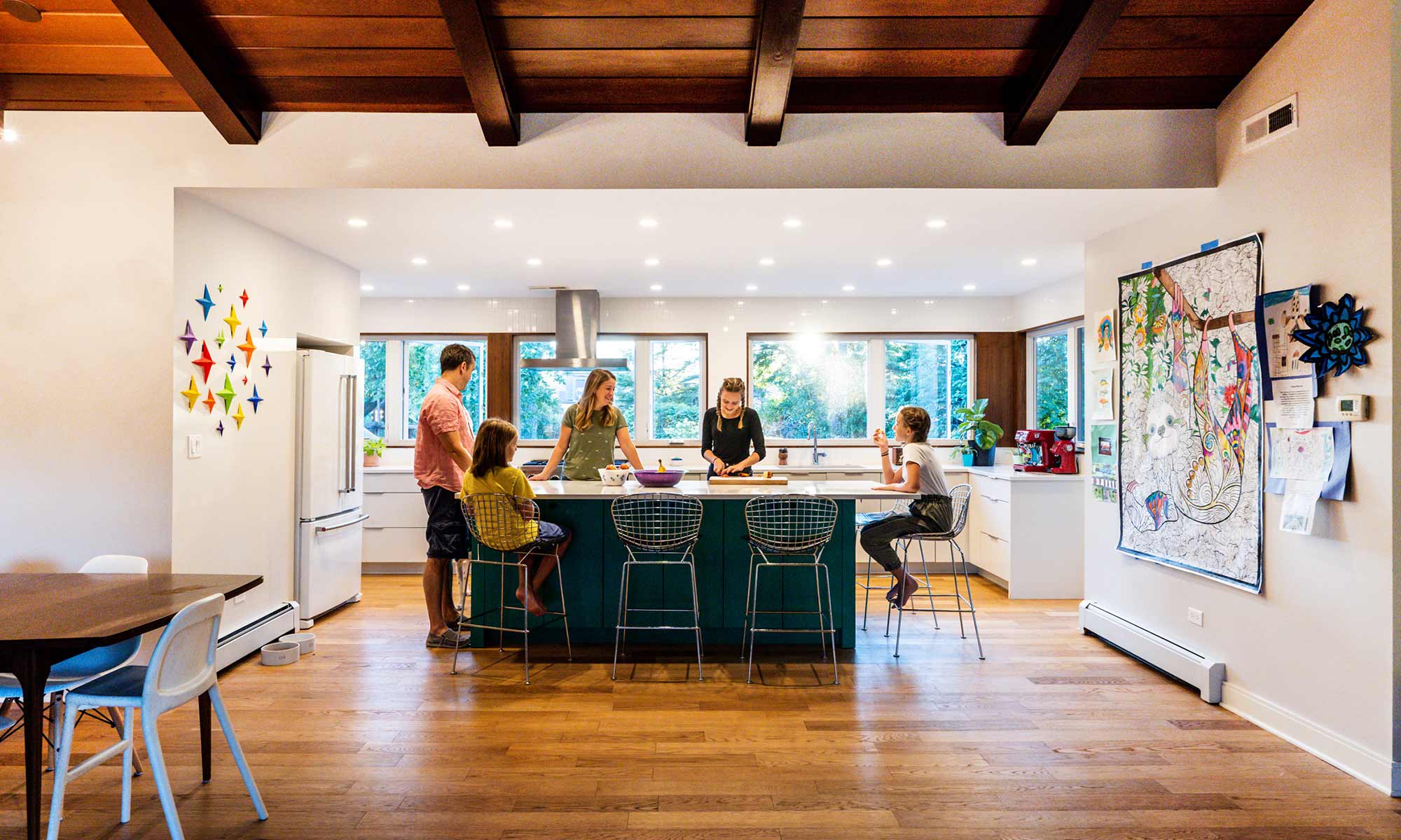 family standing around a green kitchen island in a mid century modern luxury addition wiuth sun coming through windows