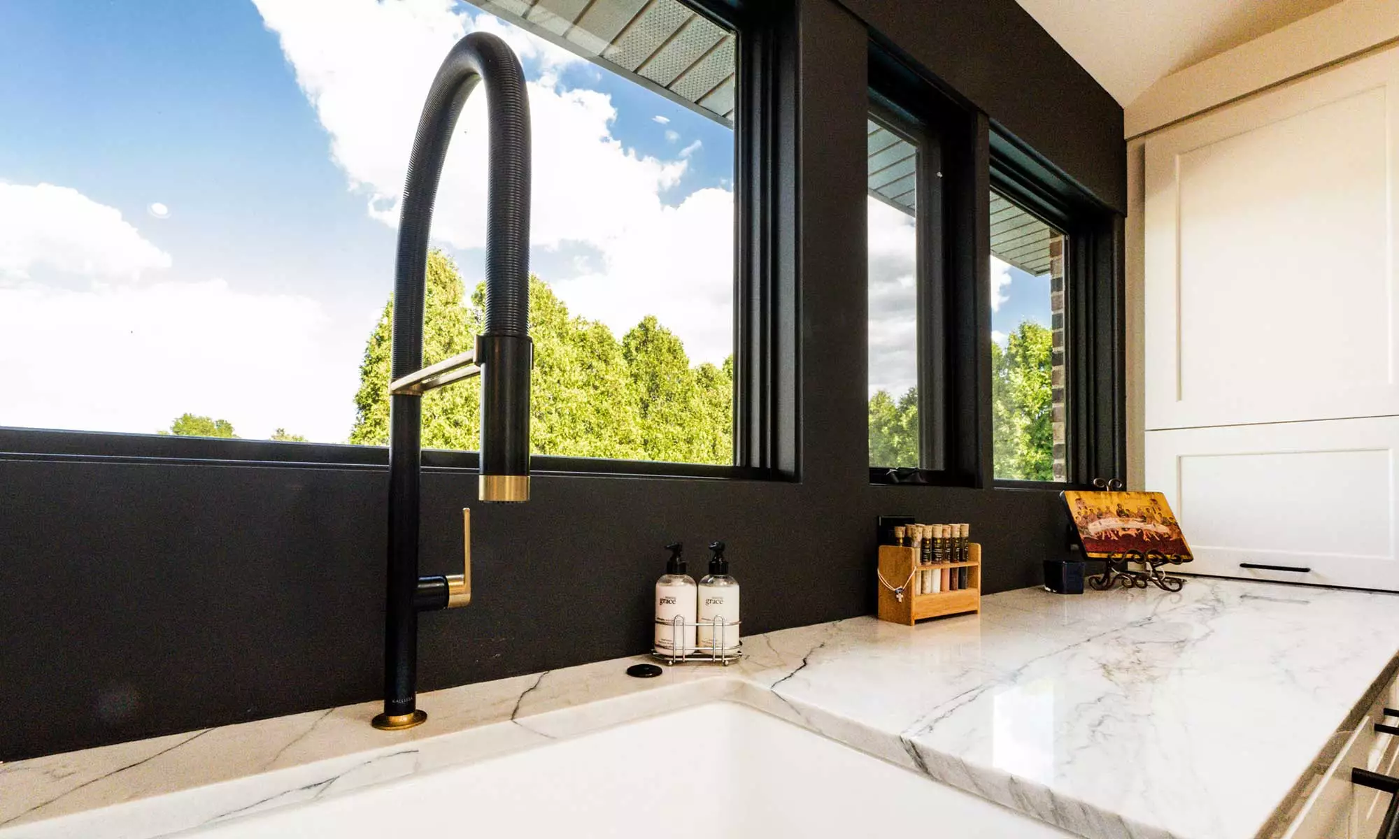 closeup view of kitchen sink faucet with windows behind and treetops