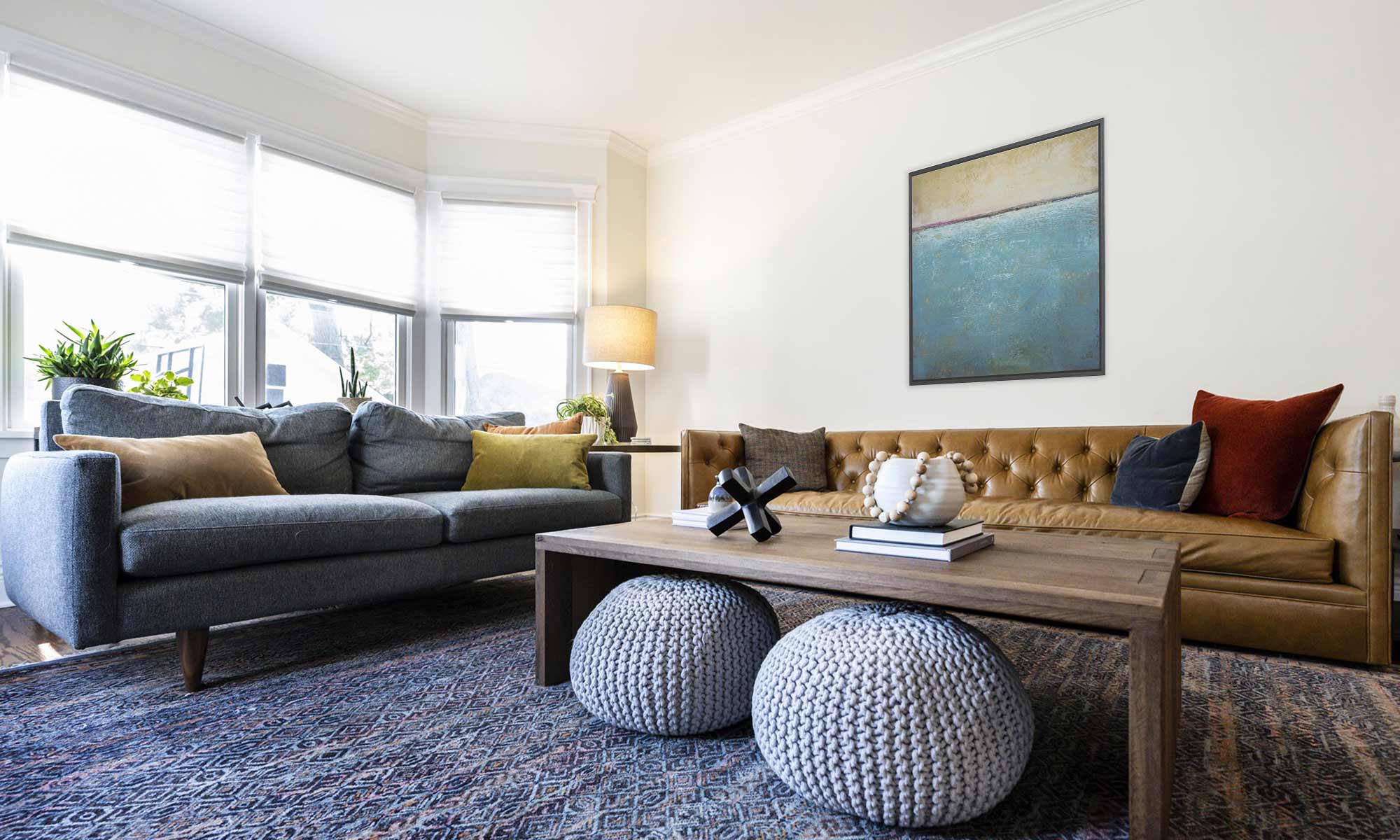 Updated Madison living room with multi-tone blue rug, light brown leather couch, & light-grained coffee table with nested grey poufs