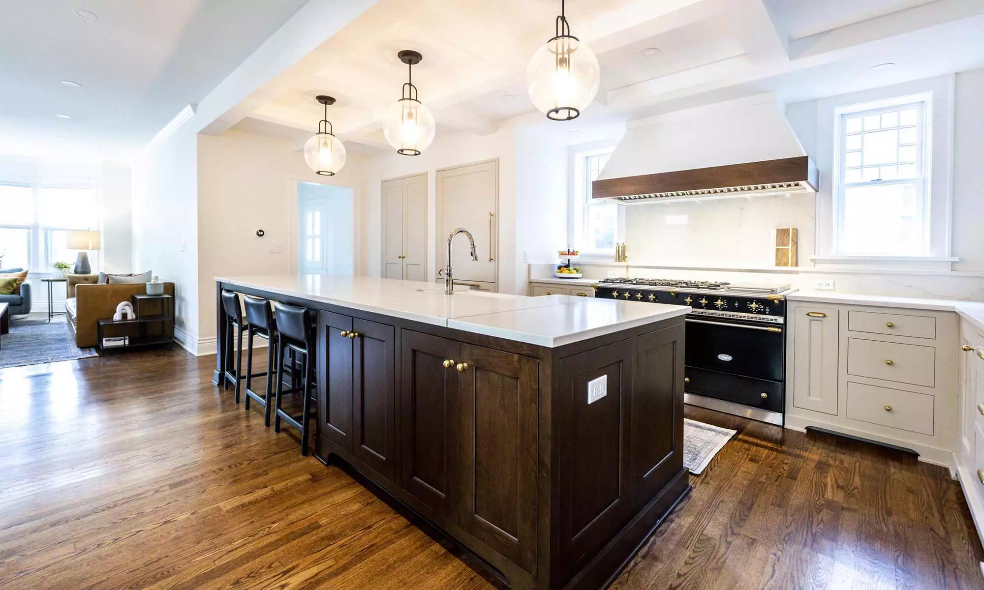 Updated Madison kitchen with dark wood-stained island, custom white cabinets & wood-edged fume hood, & black double ovens with gold accents