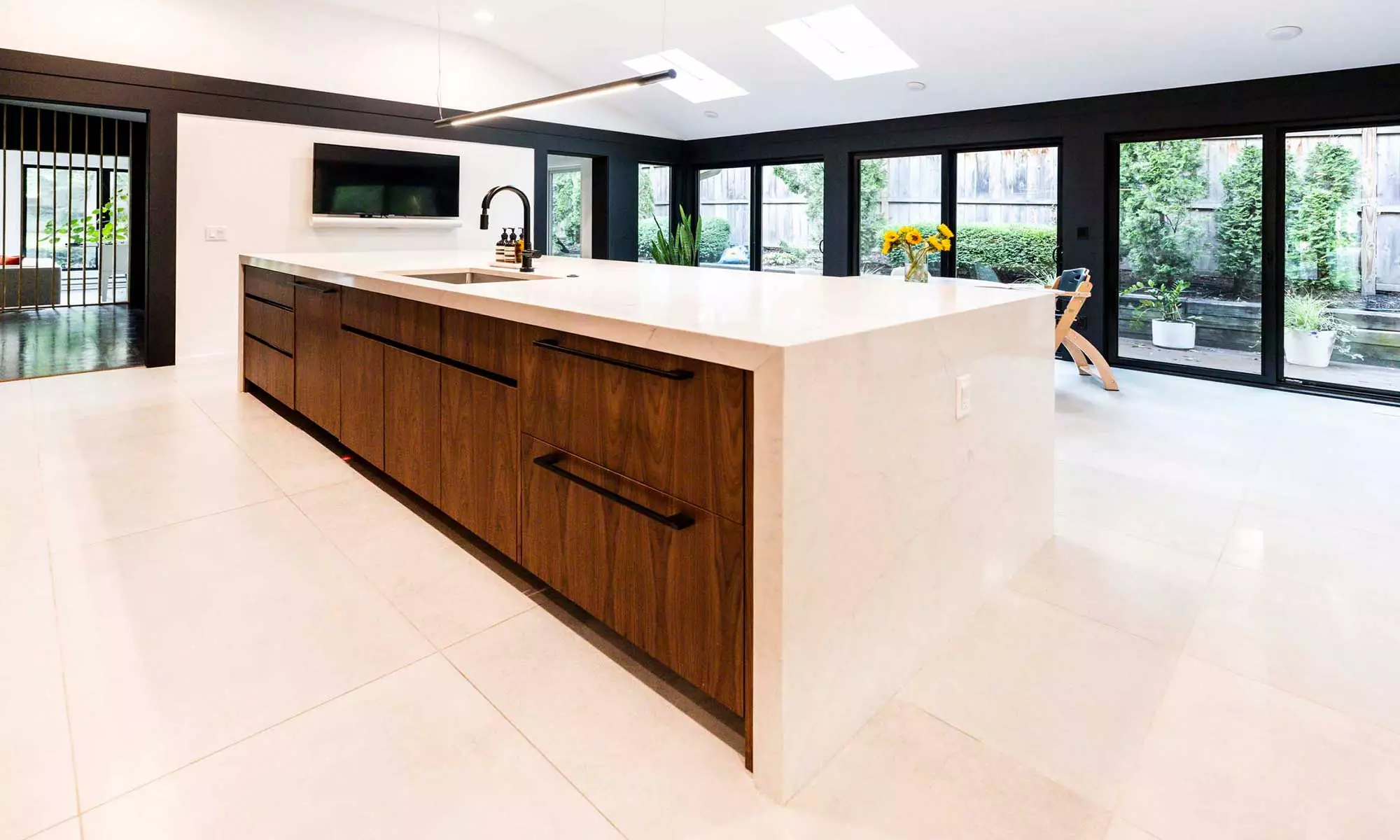 Wide view of updated Hinsdale kitchen with stained wood, white granited wrapped island, white-tiled floor, & bold black window wall