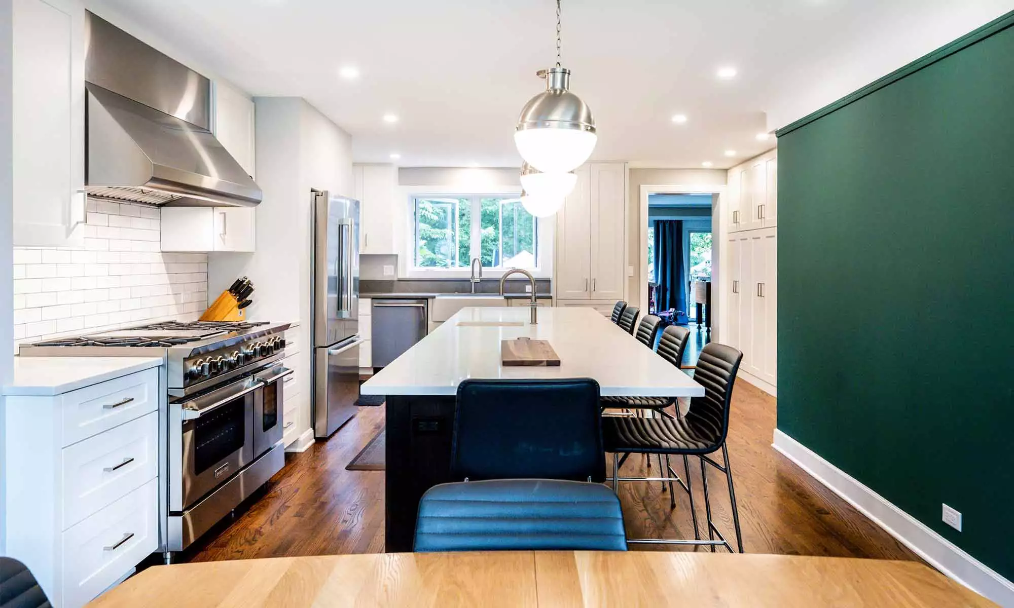 Long view of light-toned updated kitchen with new stainless steel appliances & dark green accent wall on the right