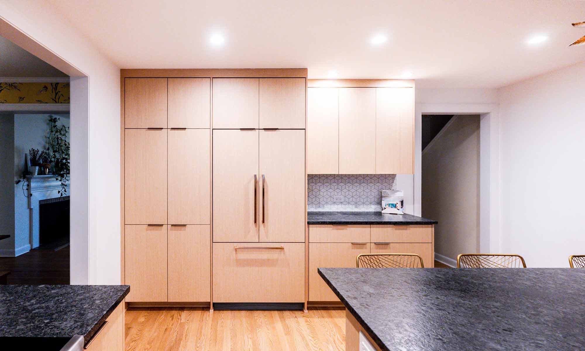 Modern luxury kitchen remodel in Riverside, IL with white oak cabinets and black stone countertops looking at builtin fridge with wood doors