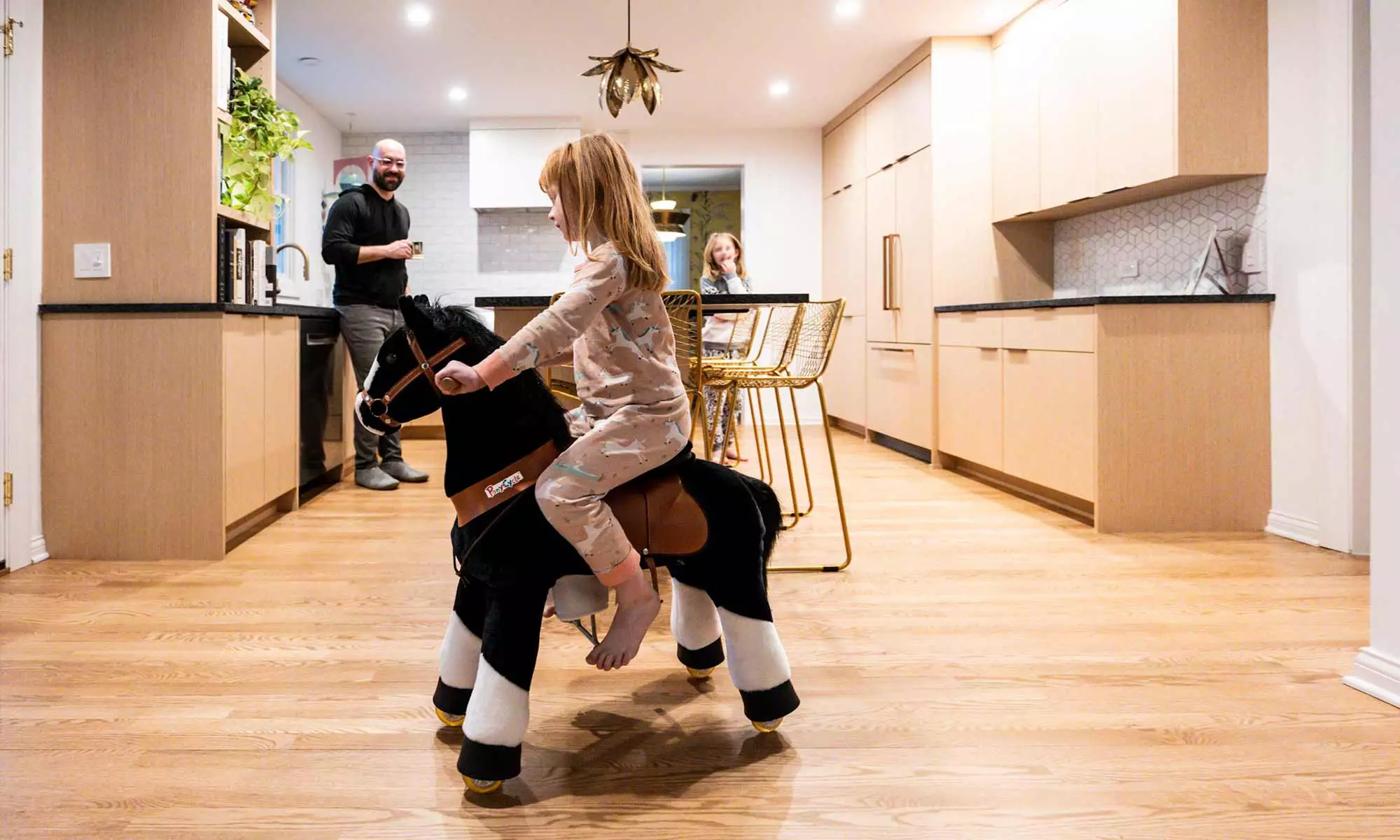 Family gathered around white oak island with black stone countertops in luxury Riverside, IL kitchen remodel with daughter riding toy horse