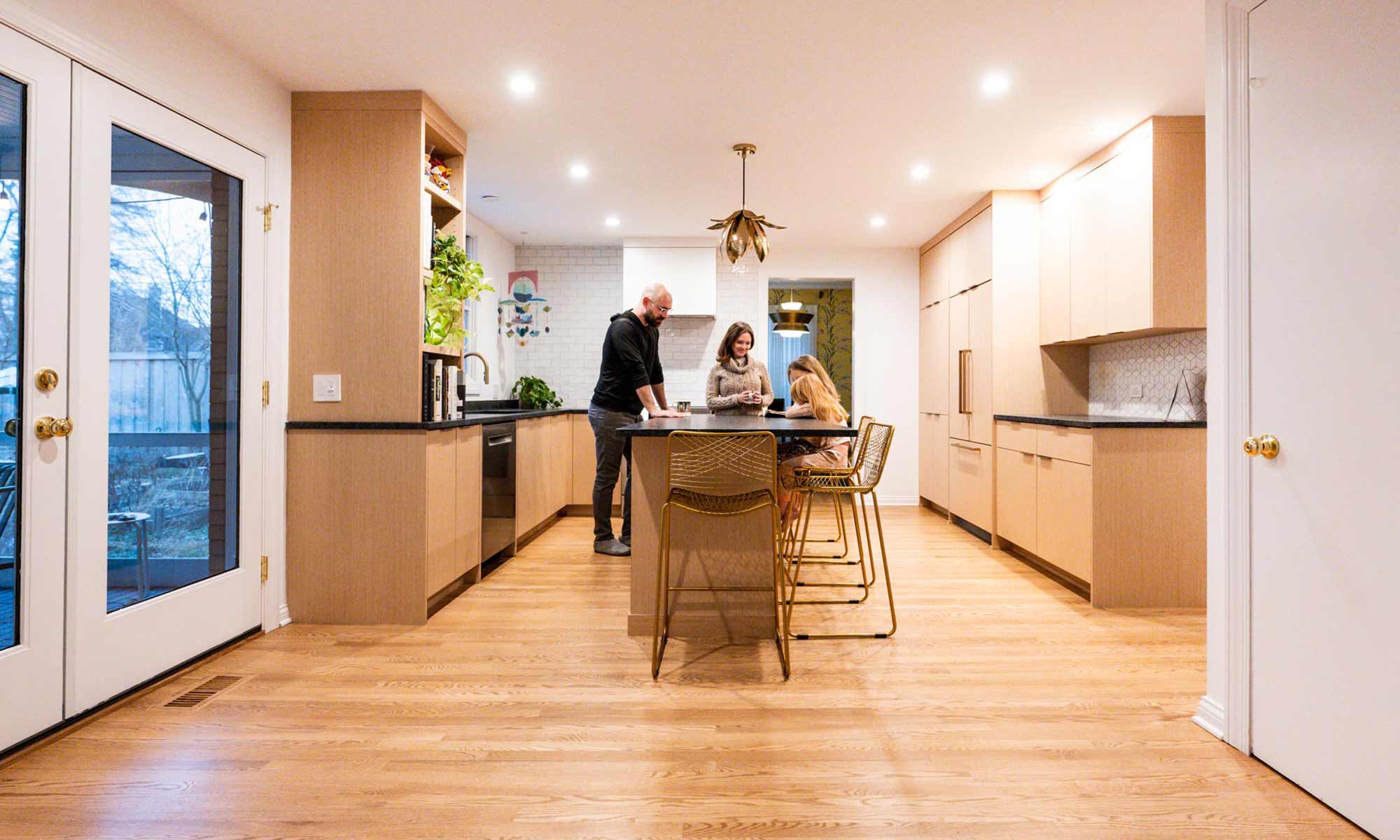 Family gathered around white oak island with black stone countertops in luxury Riverside, IL kitchen remodel with rondelay mobile in corner