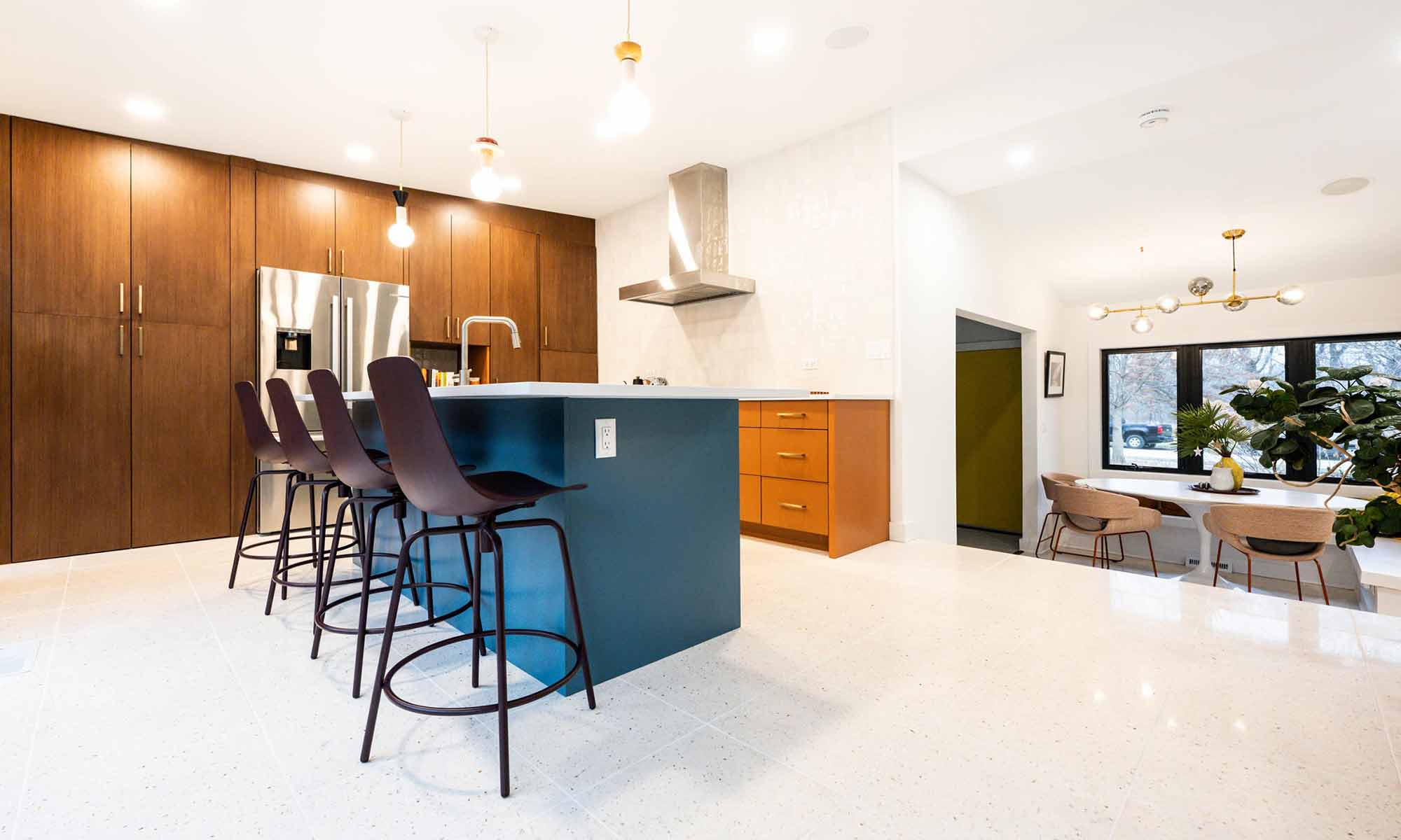 Mid century modern luxury kitchen remodel in Riverside IL by LivCo with blue island orange perimeter cabinets walnut tall cabinets and terrazzo flooring looking down towards breakfast area