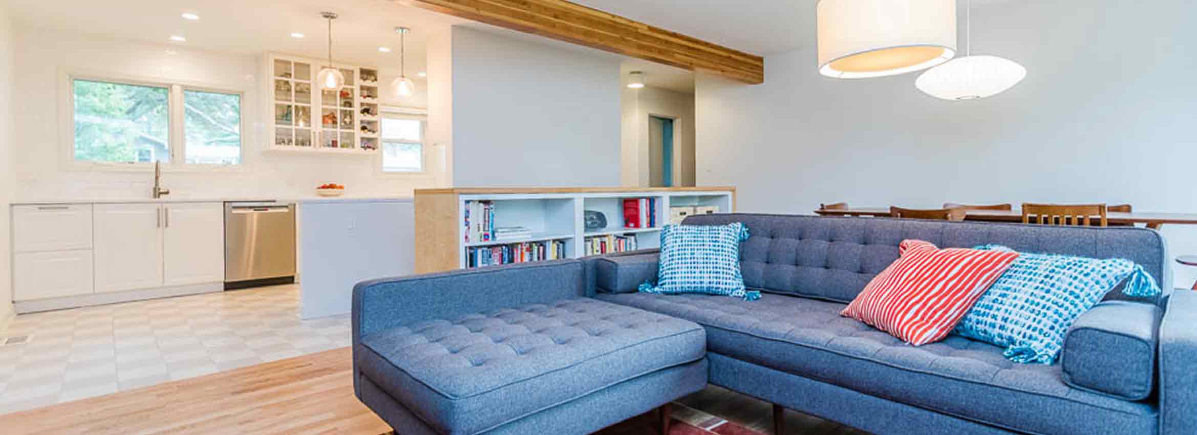 mid century modern home remodel view from living room to kitchen with open plan exposed wood beam and blue grey sectional sofa