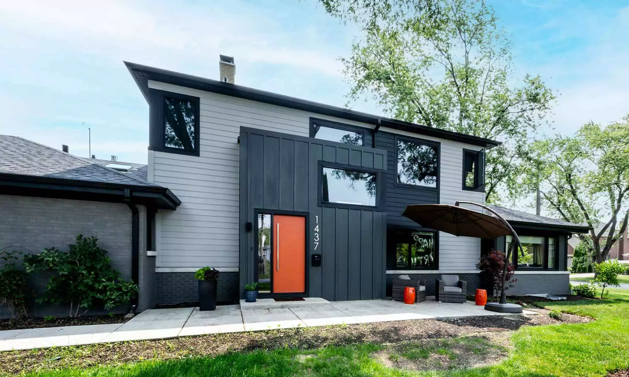 exterior view of modern luxury second story addition with grey siding and black windows and orange door