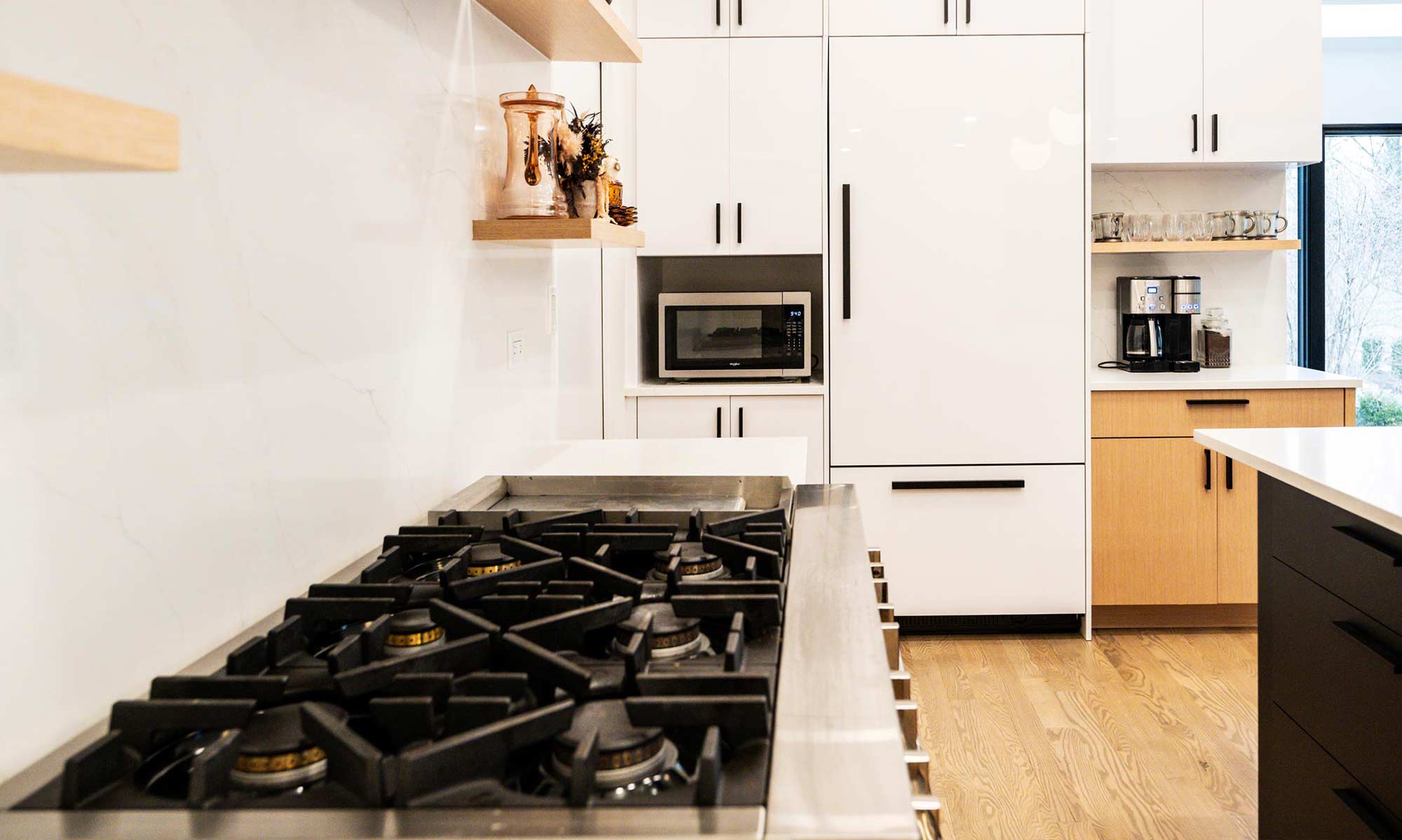 Indian Head Park luxury kithcen remodel by LivCo featuring wood, black, and gloss white modern cabinetry with view towards built-in fridge looking over 48 inch gas range