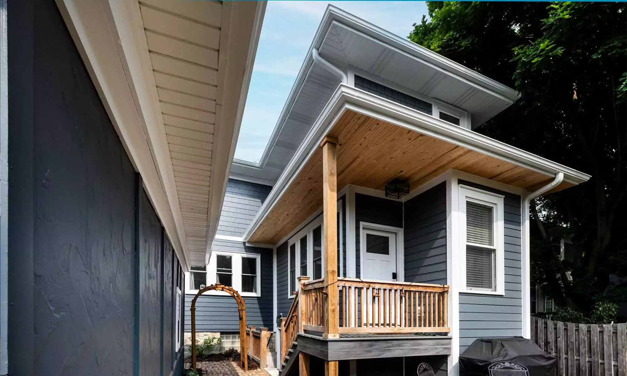 Exterior view of vintage addition with dark blueish grey siding, white windows, and cedar porch