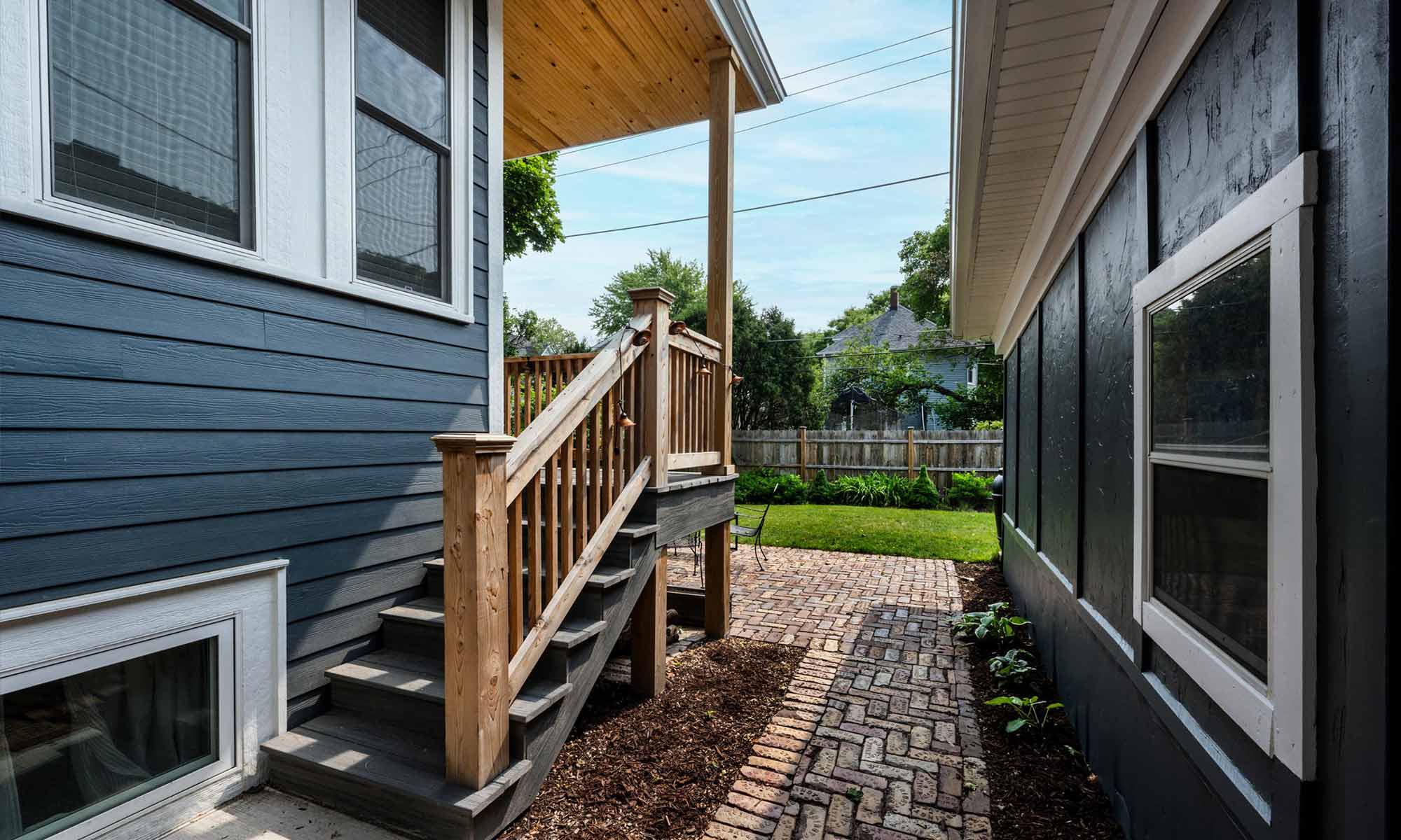 Exterior view of vintage addition with dark blueish grey siding, white windows, and cedar porch