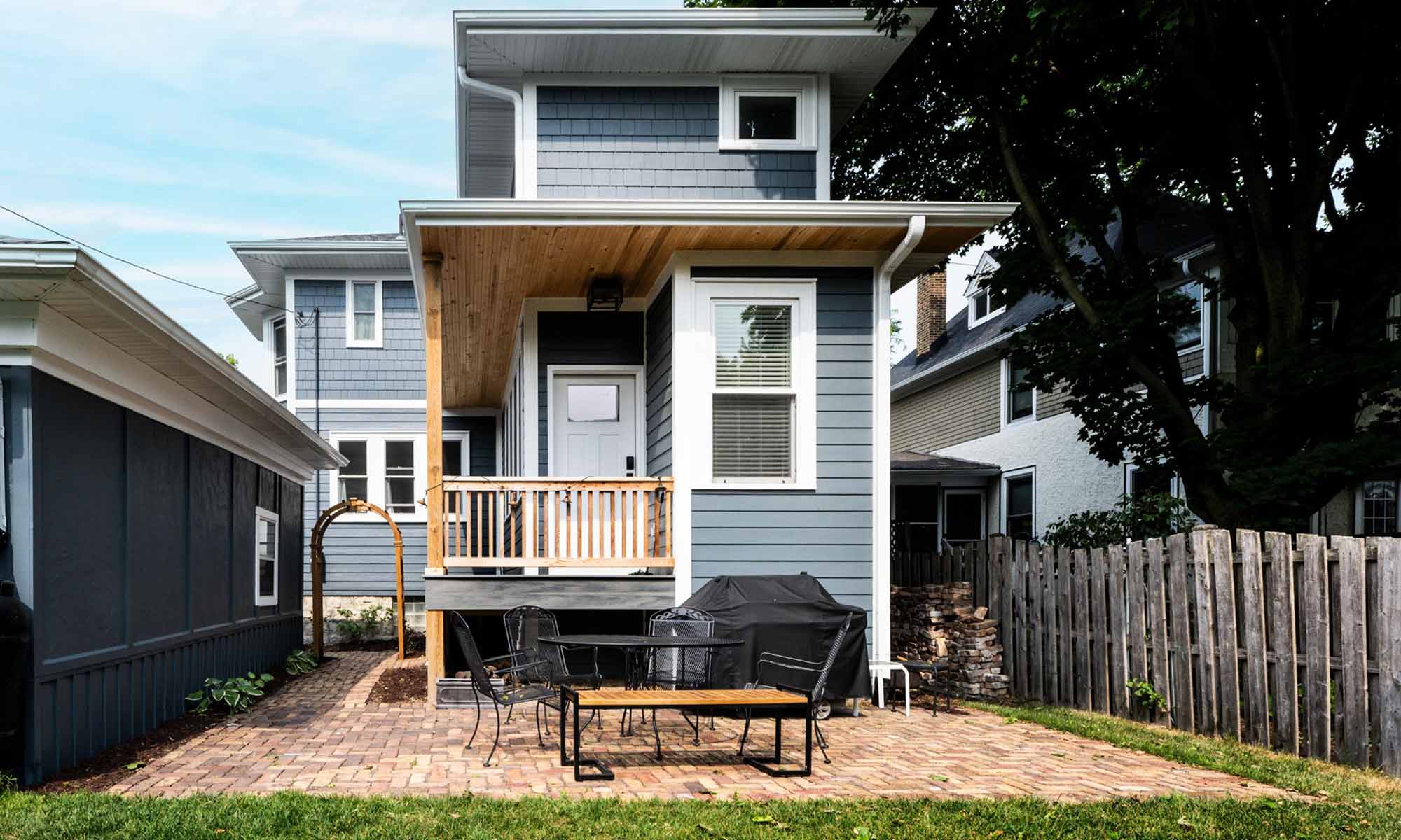 Exterior view of vintage addition with dark blueish grey siding, white windows, and cedar porch