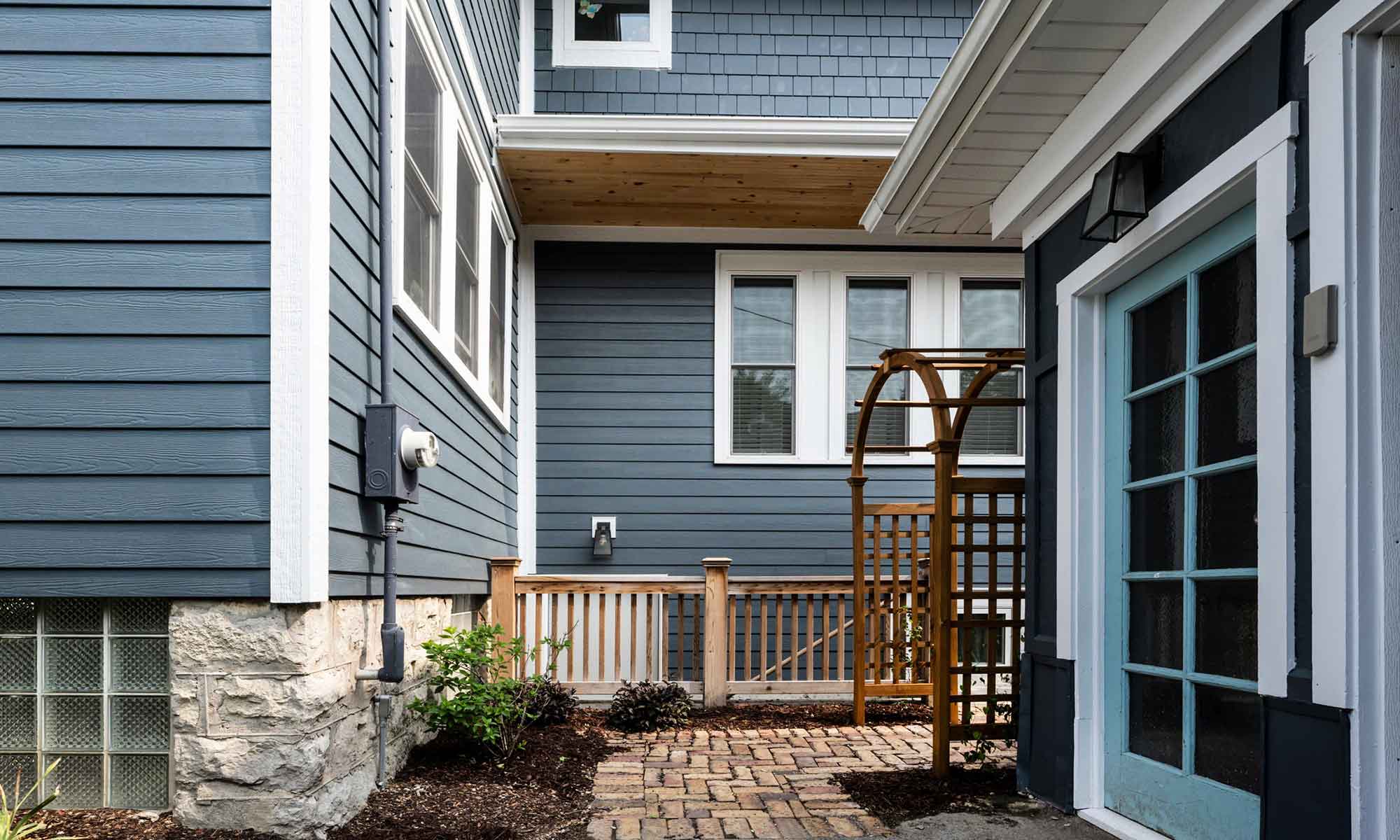 Exterior view of vintage addition with dark blueish grey siding, white windows, and cedar porch