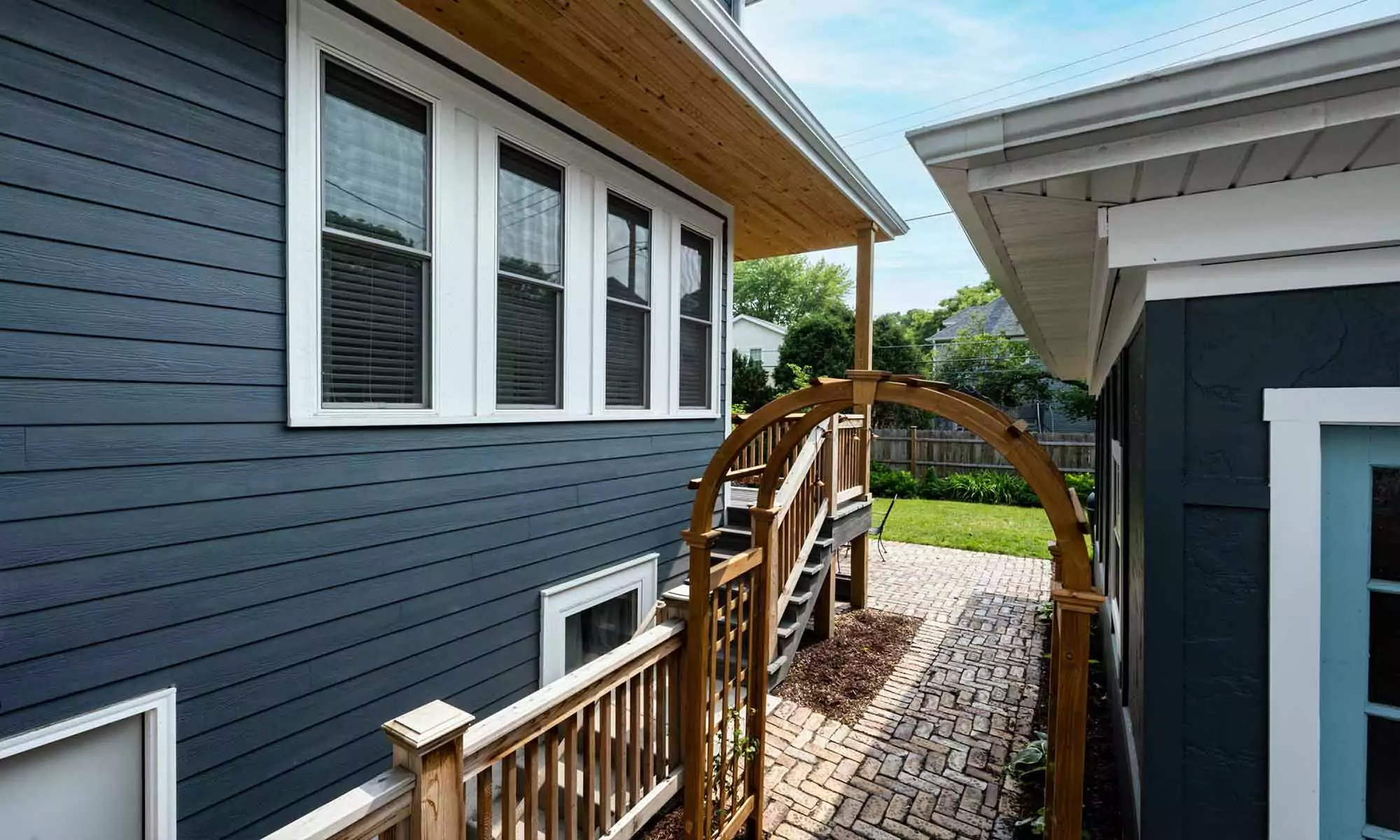 Exterior view of vintage addition with dark blueish grey siding, white windows, and cedar porch