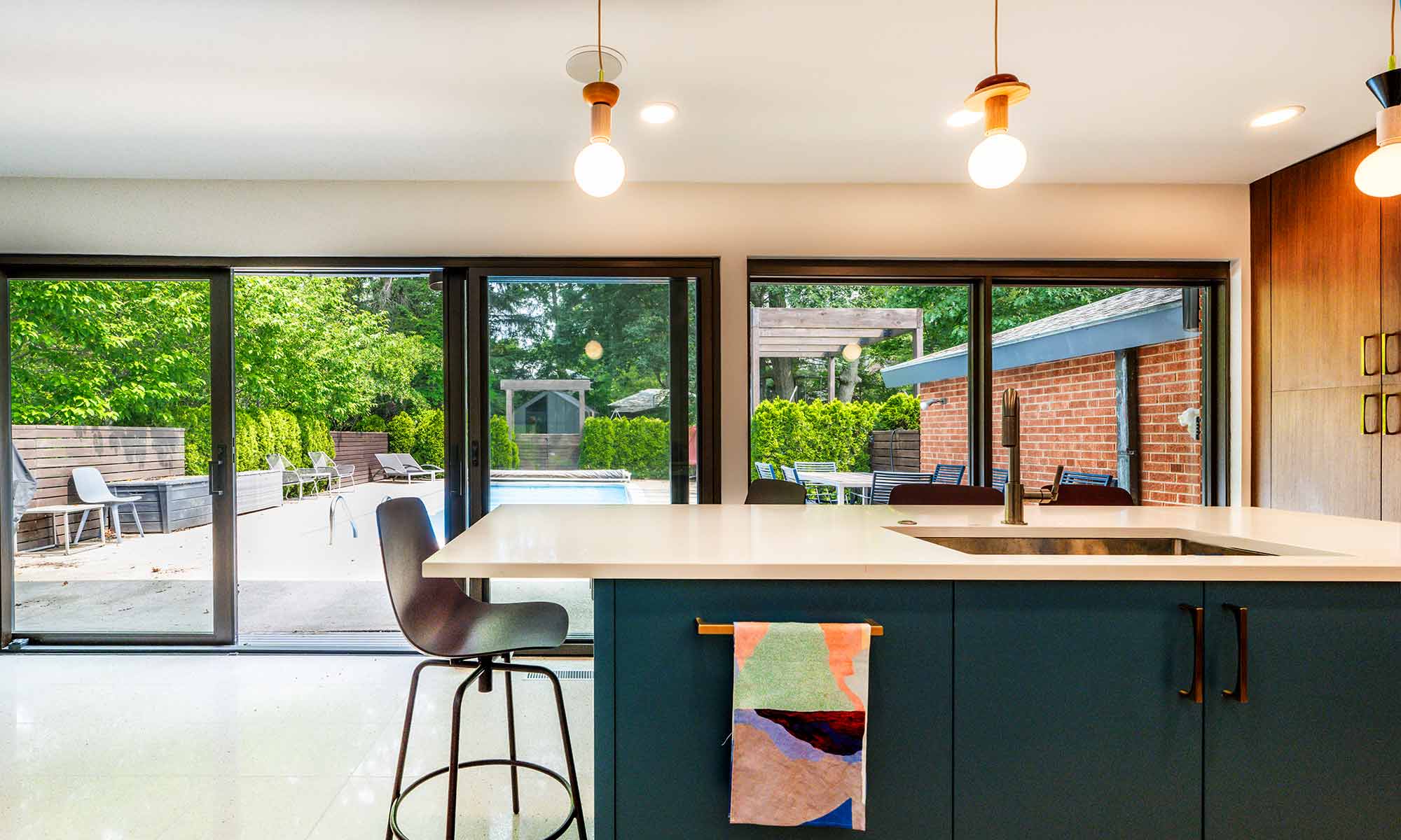 Blue kitchen island looking out to backyard pool area in luxury mid century modern kitchen remodel in Riverside IL designed and built by LivCo