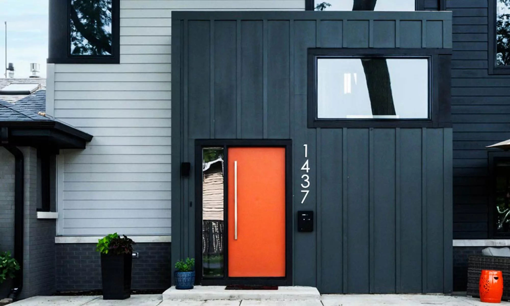 exterior view of entrance of modern luxury second story addition with grey siding and black windows and orange door