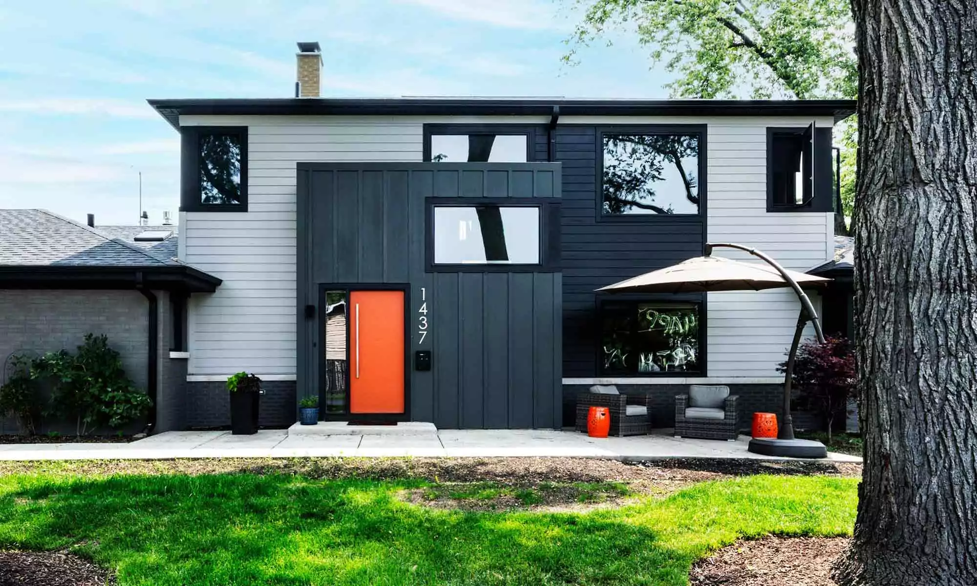 exterior view of modern luxury second story addition with grey siding and black windows and orange door