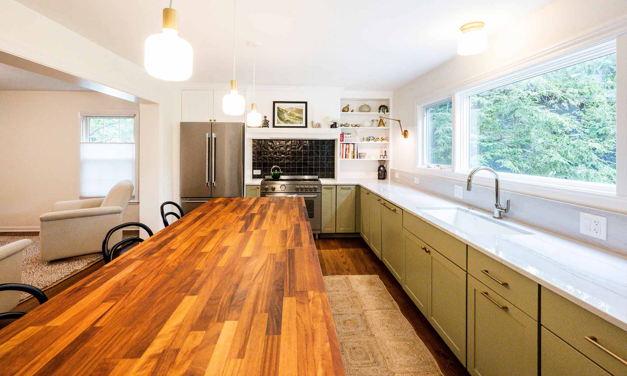 luxury kitchen remodel with green cabinets and butcherblock island and black backsplash tile behind the range