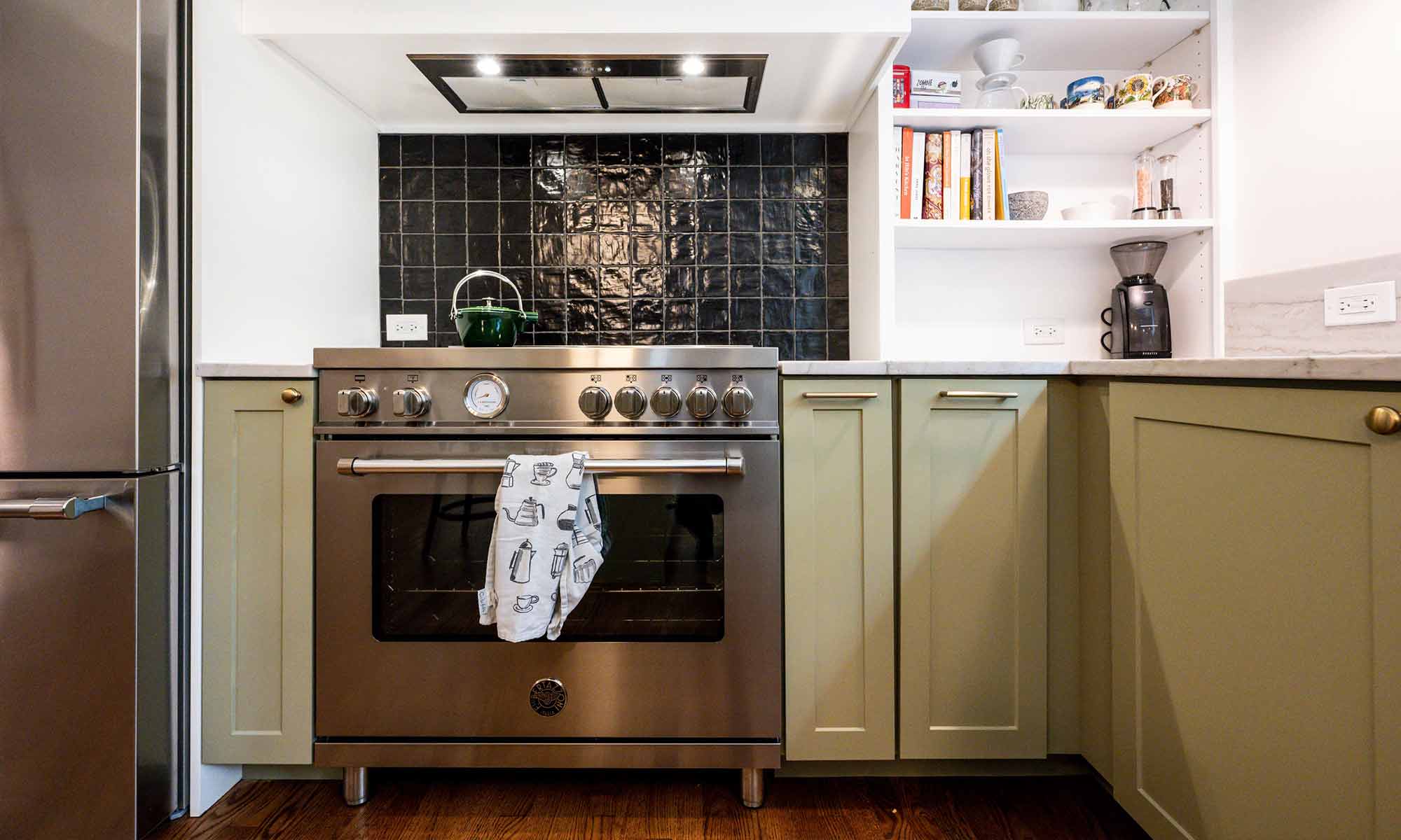 closeup view of stainless steel range and black backsplash tile in luxury kitchen remodel with green cabinets