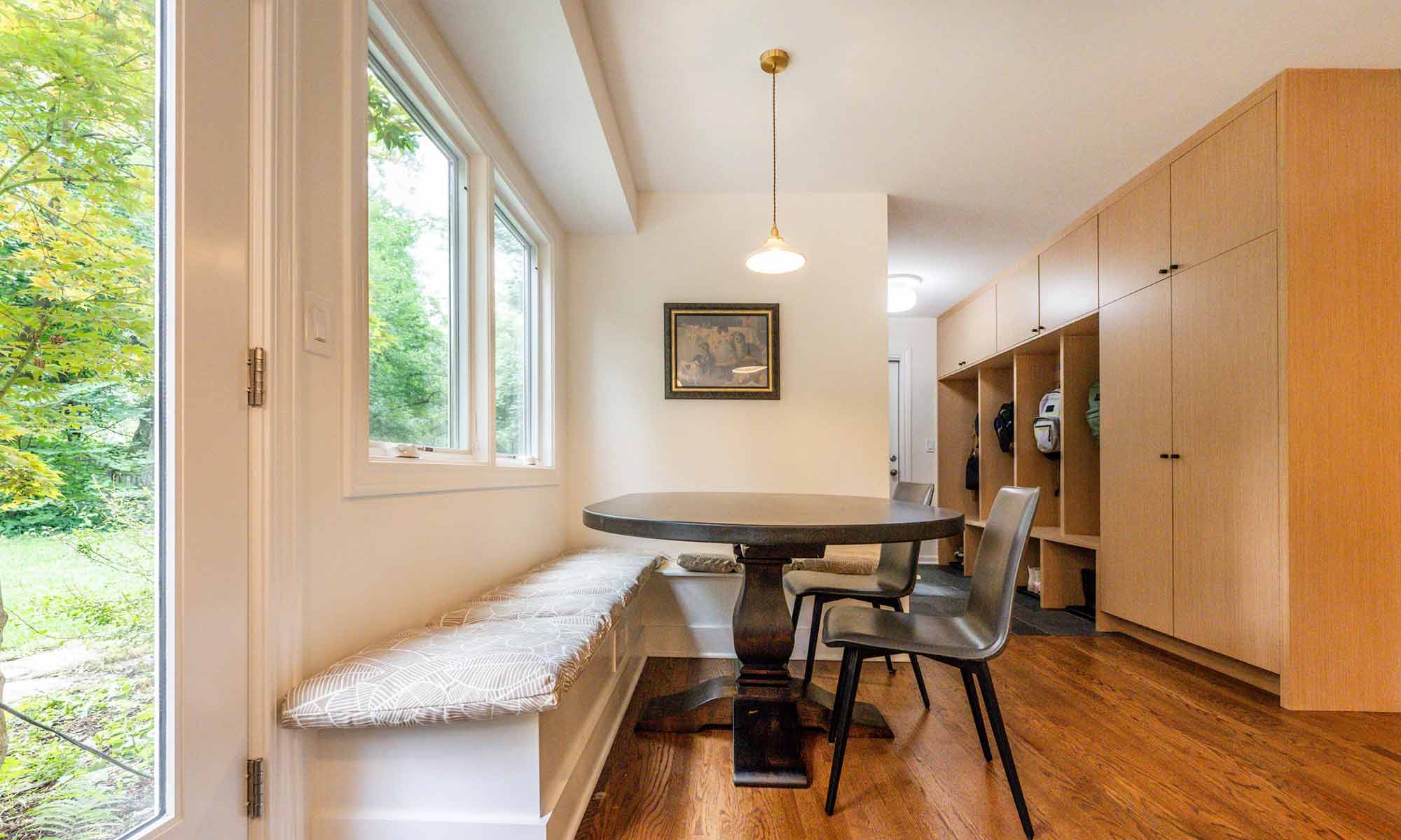 Built-in banquette seating under window in luxury kitchen remodel with view towards mudroom built-in cabinetry
