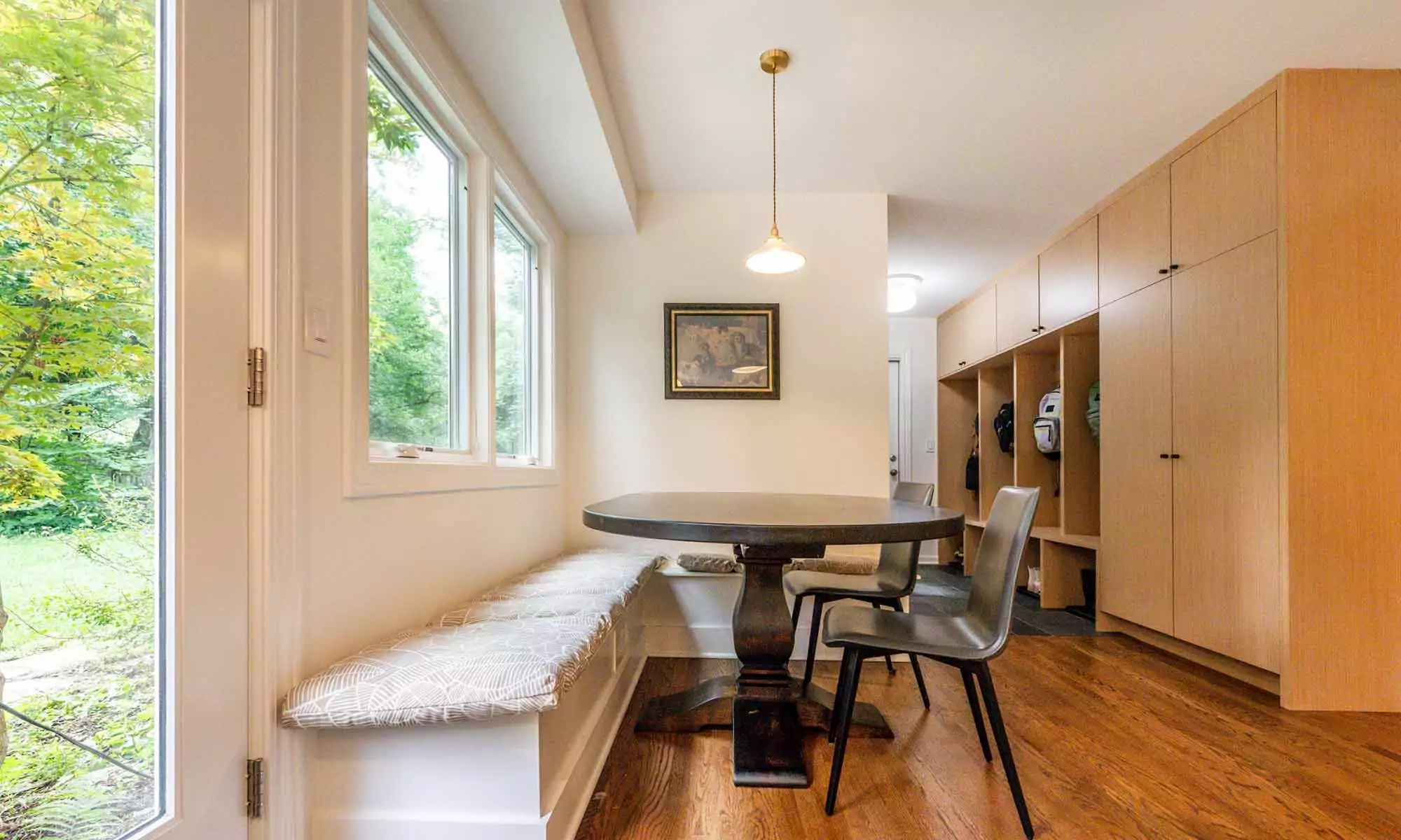 Built-in banquette seating under window in luxury kitchen remodel with view towards mudroom built-in cabinetry