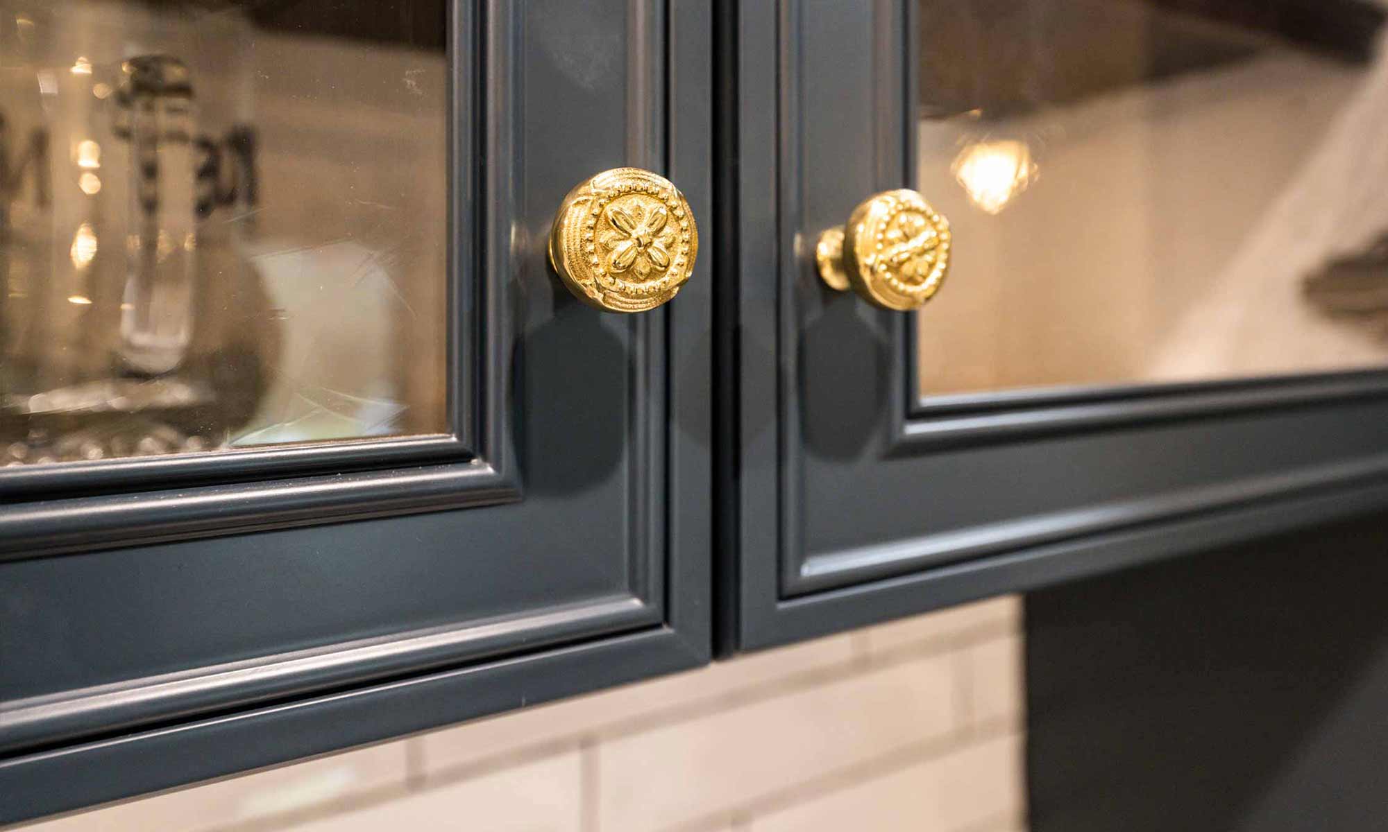 closeup of brass knobs on slate blue kitchen cabinets with glass doors