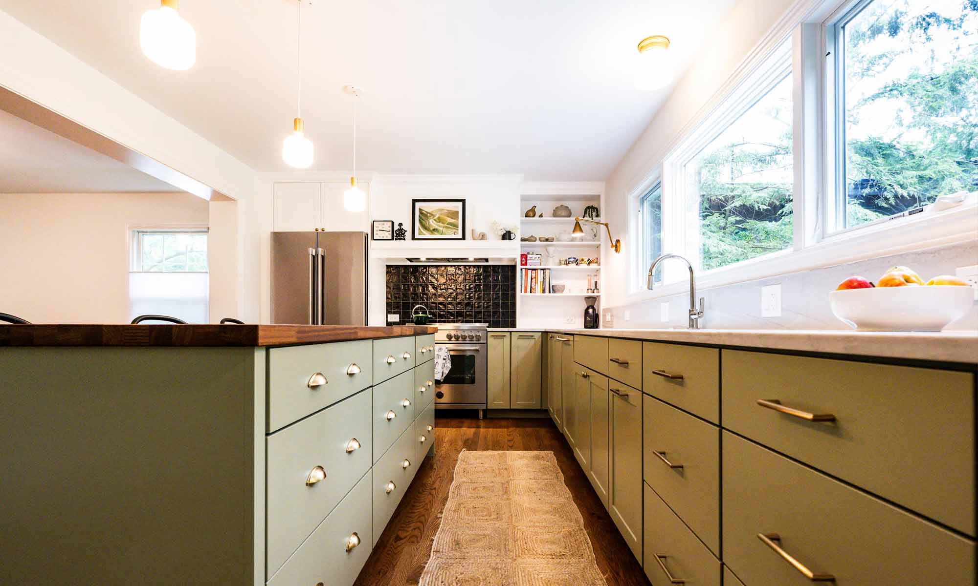 luxury kitchen remodel with green cabinets and butcherblock island and black backsplash tile behind the range