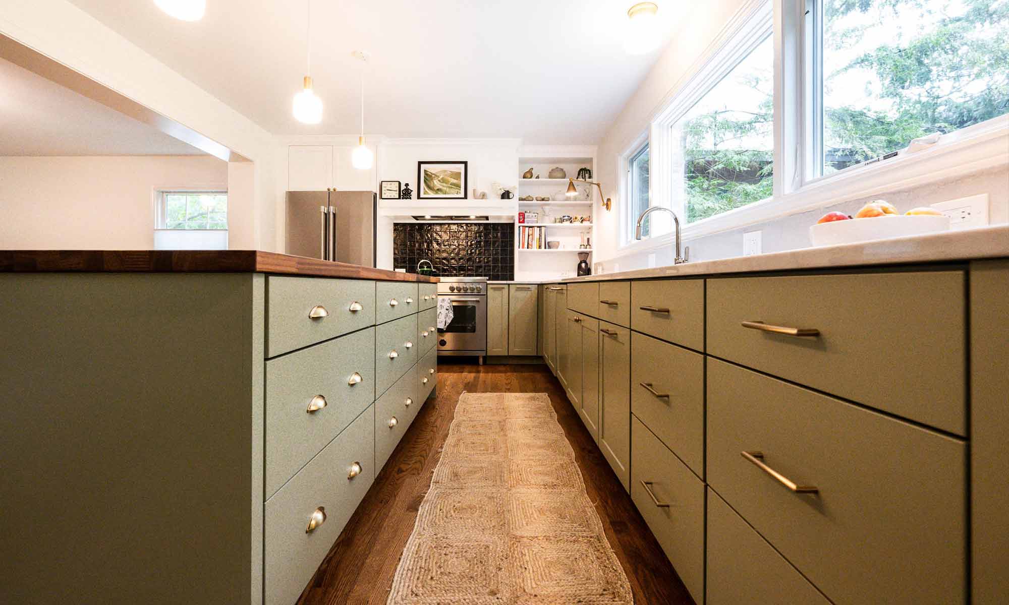 luxury kitchen remodel with green cabinets and butcherblock island and black backsplash tile behind the range