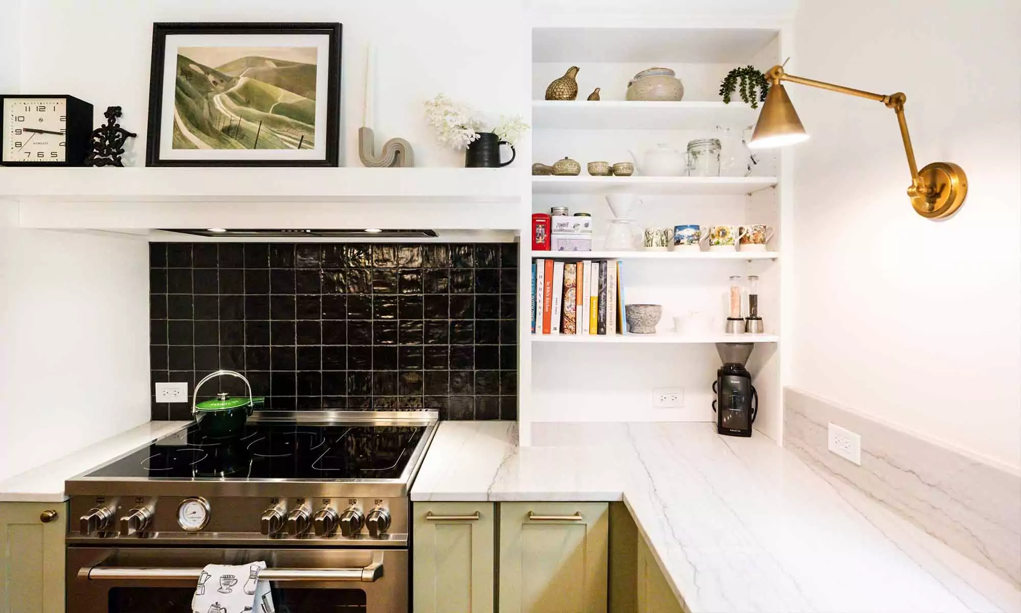 closeup view of stainless steel range and black backsplash tile in luxury kitchen remodel with green cabinets and an adjustable wall sconce