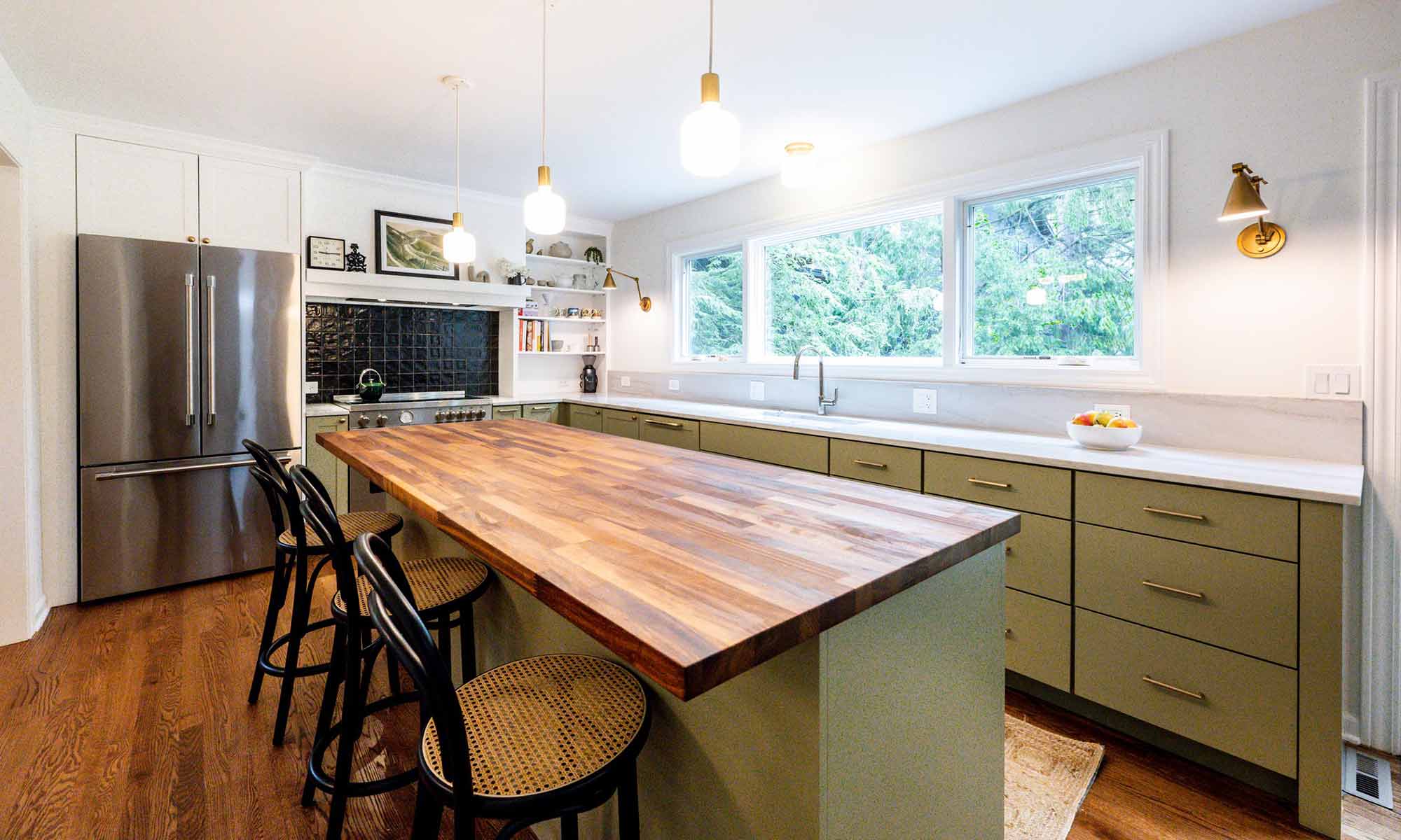luxury kitchen remodel with green cabinets and butcherblock island and three stools looking out towards backyard