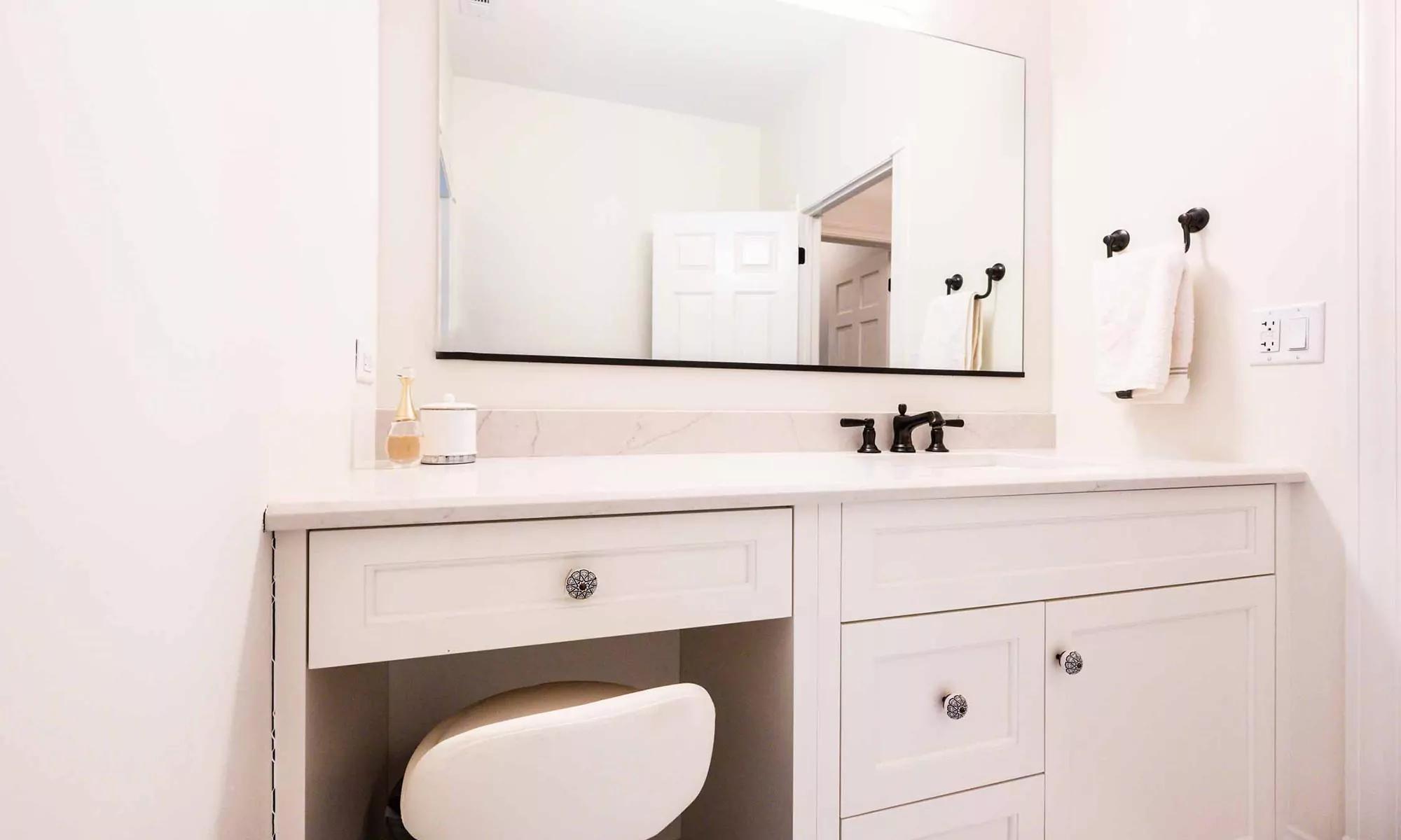 makeup station in luxury bath remodel with white cabinets and mirror