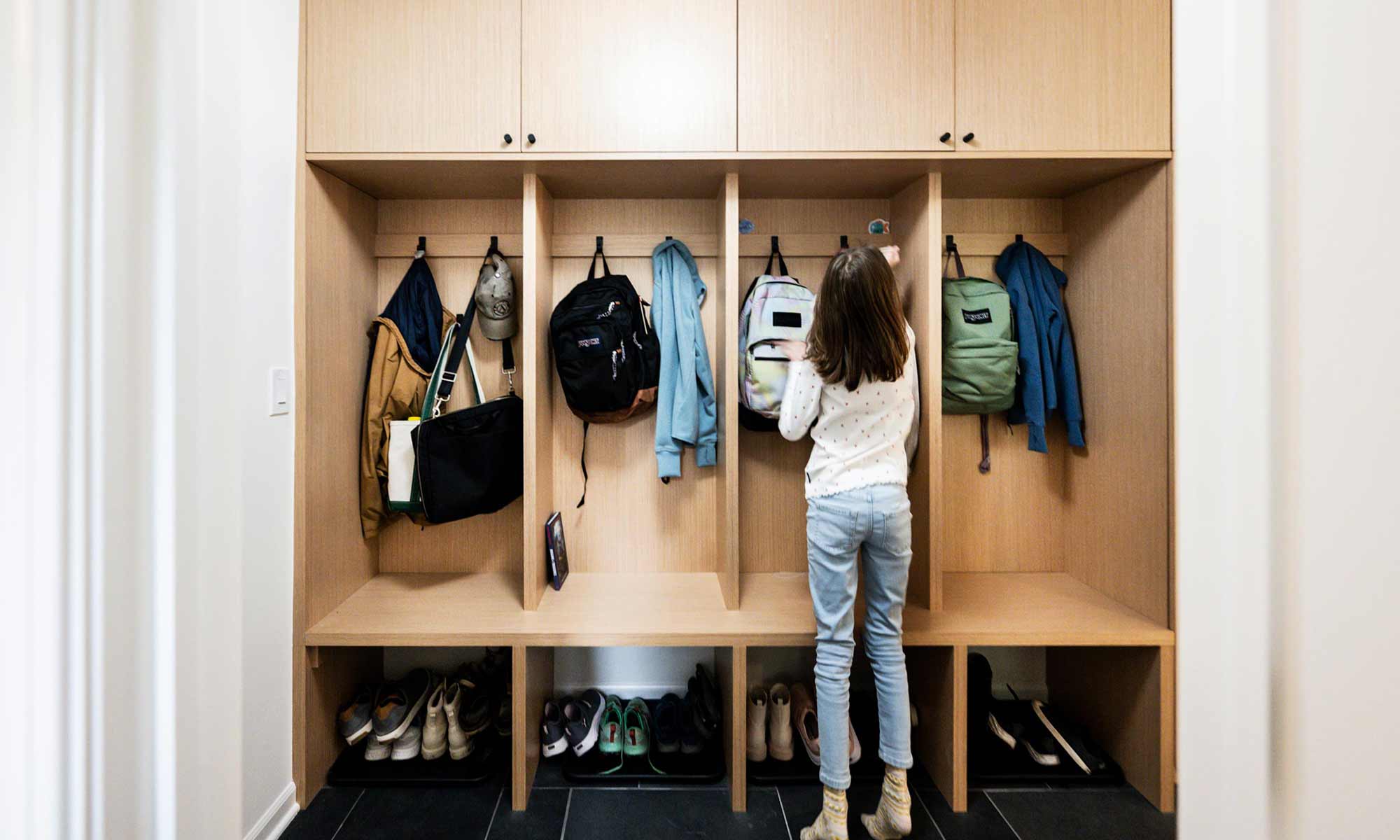 white oak mudroom built-ins in luxury home remodel and girl hanging up backpack