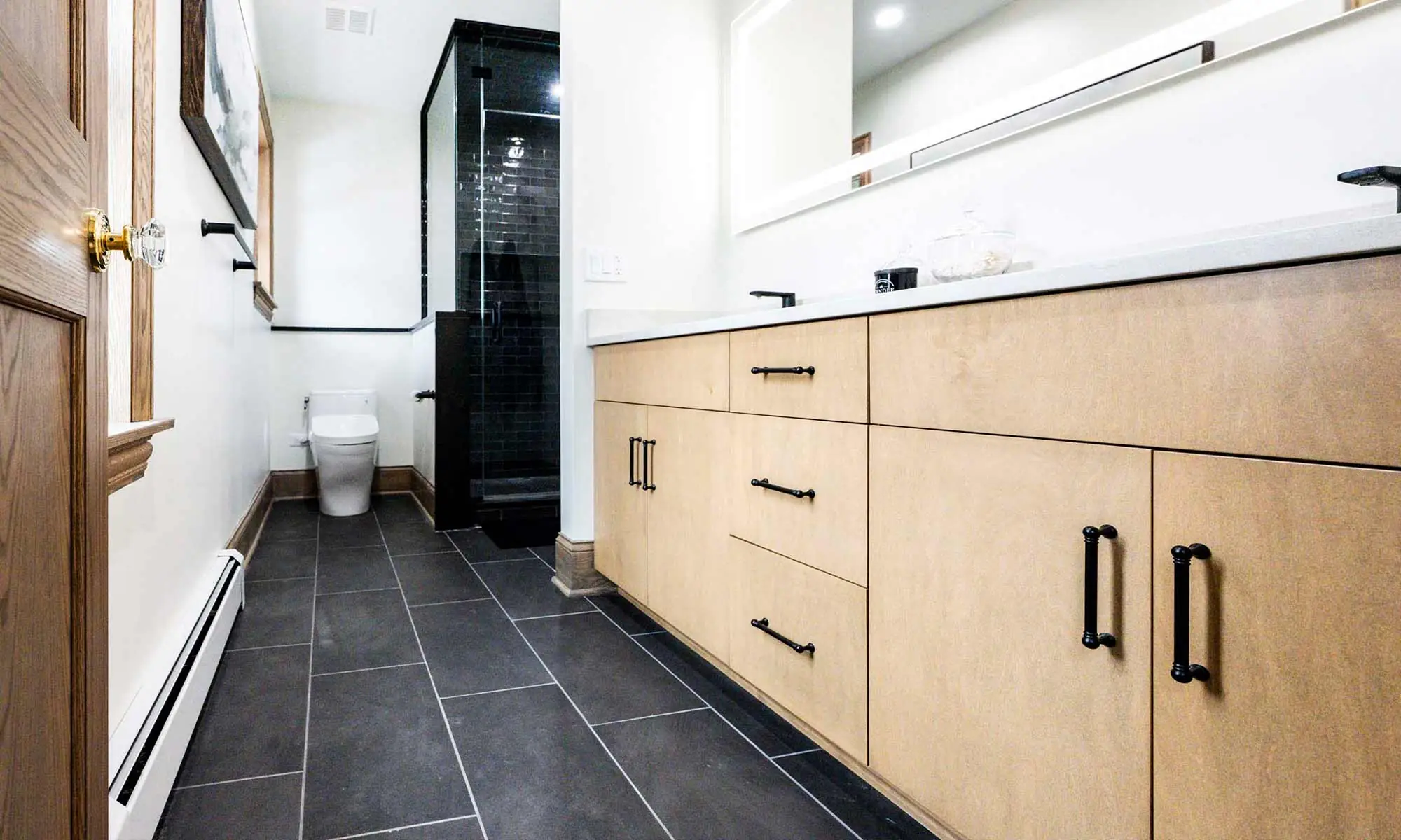 luxury bathroom remodel with light wood cabinets and black plumbing fixtures and lighted mirror