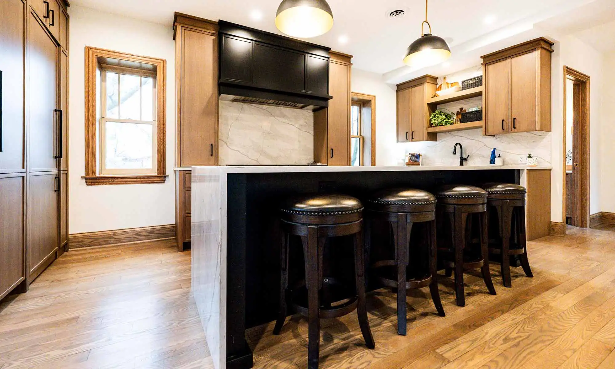 view of luxury kitchen remodel with windows flanking large range wall and white oak cabinetry and island bar seating