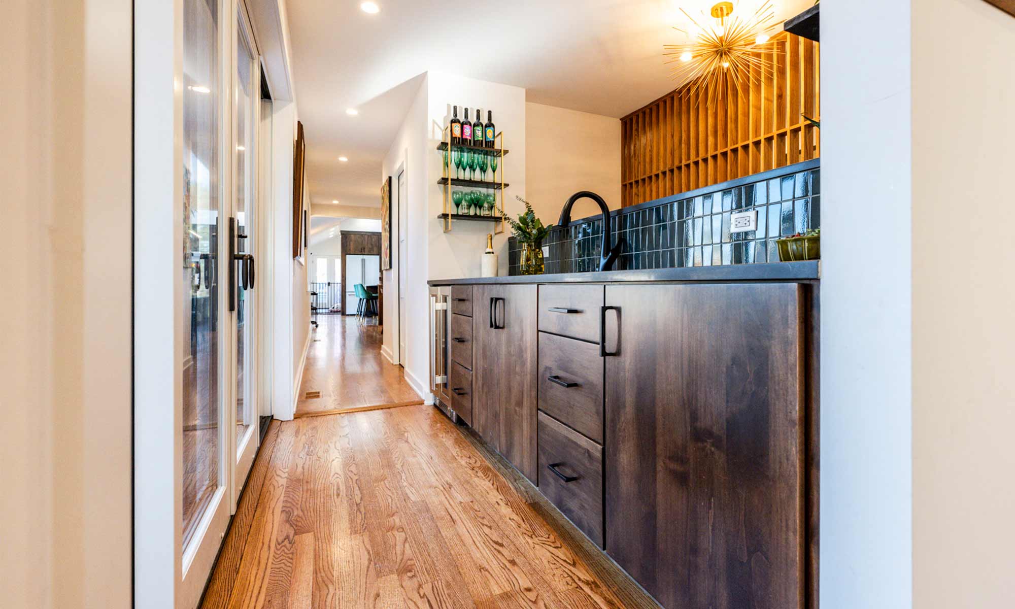 dark wood cabinets with black handles and faucet at aa modern open wet bar. also has open shelves with bottles and glass, and an open wooden feature wall in the background