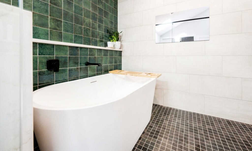A stylish bathroom adorned with green tiles and a pristine white tub, offering a serene and modern aesthetic.