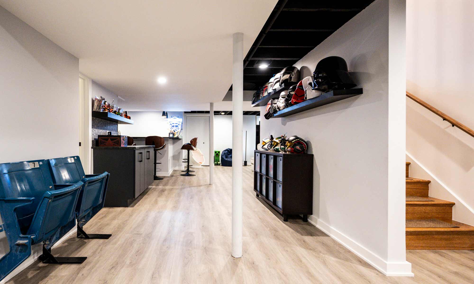 Finished basement with light wood flooring, sports memorabilia display, modern bar, and vintage stadium seats.