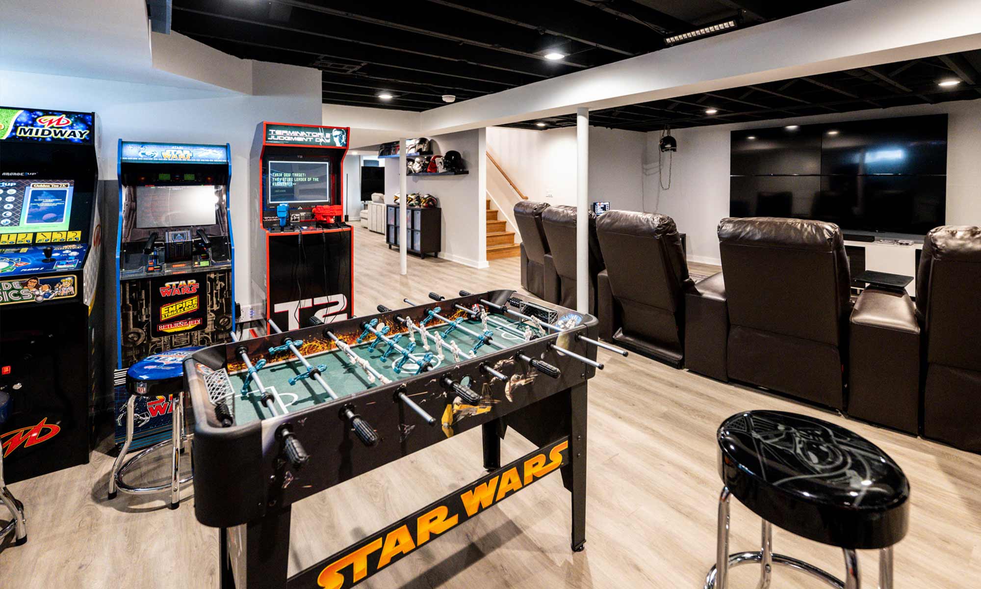 Basement game room with vintage arcade machines, Star Wars foosball table, home theater seating, and large TV wall.