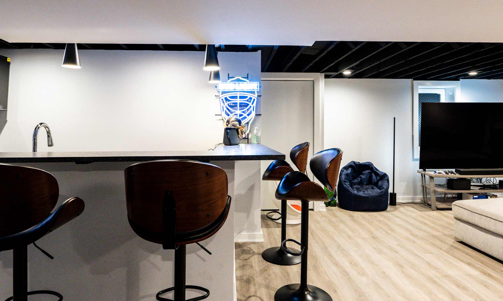 Basement entertainment area with bar seating, bean bag chair, large flat-screen TV, and minimalist decor.
