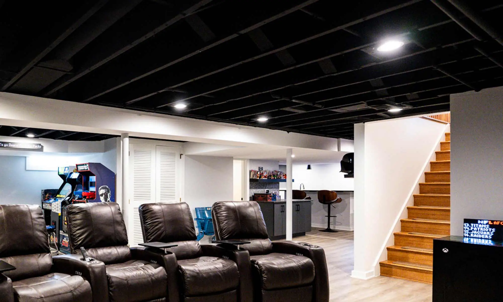 Finished basement with theater seating, black ceiling beams, and open view of arcade and bar areas.
