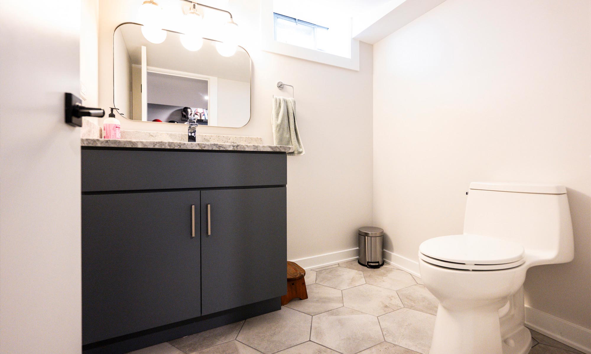 Contemporary basement bathroom with hexagonal floor tile, modern vanity with quartz countertop, and backlit mirror.