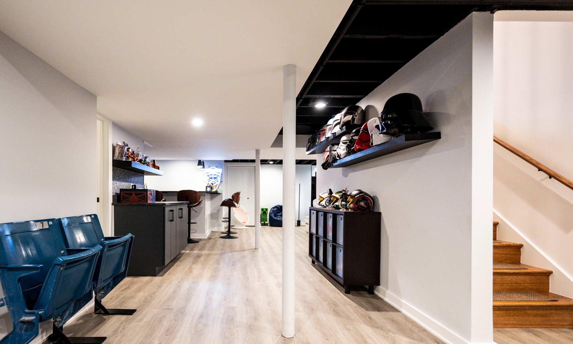 Finished basement with wood flooring, stadium seating, modern bar, and sports memorabilia display with helmets and collectibles.
